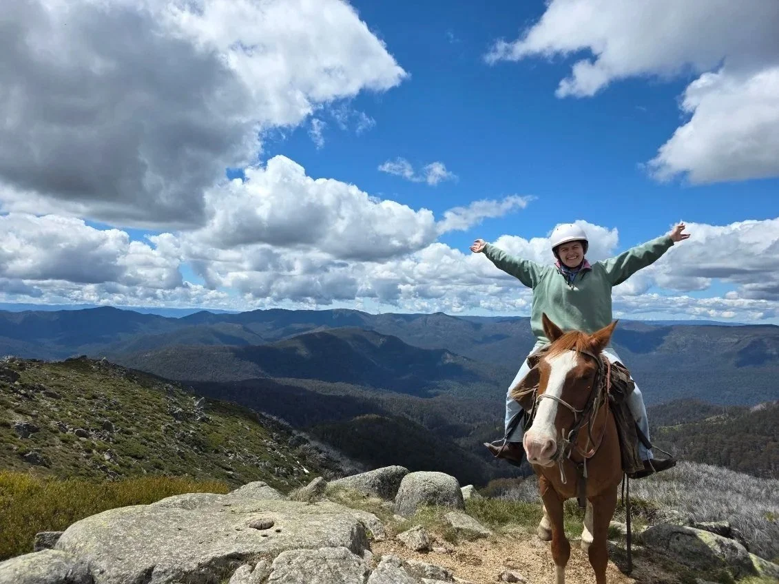 Jojo sitting on chestnut horse on top of mountain with vast views of Australia