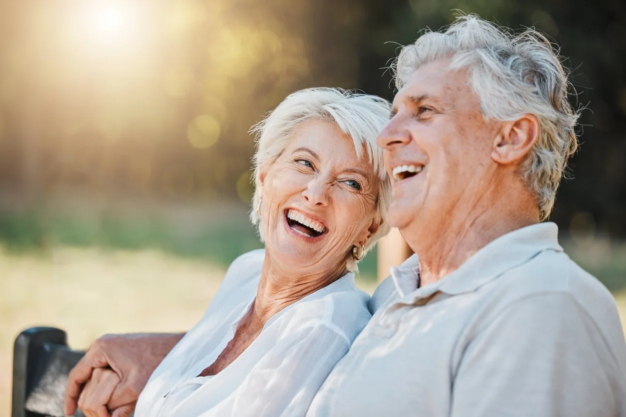 Older couple sitting outdoors, smiling and laughing together during sunset.