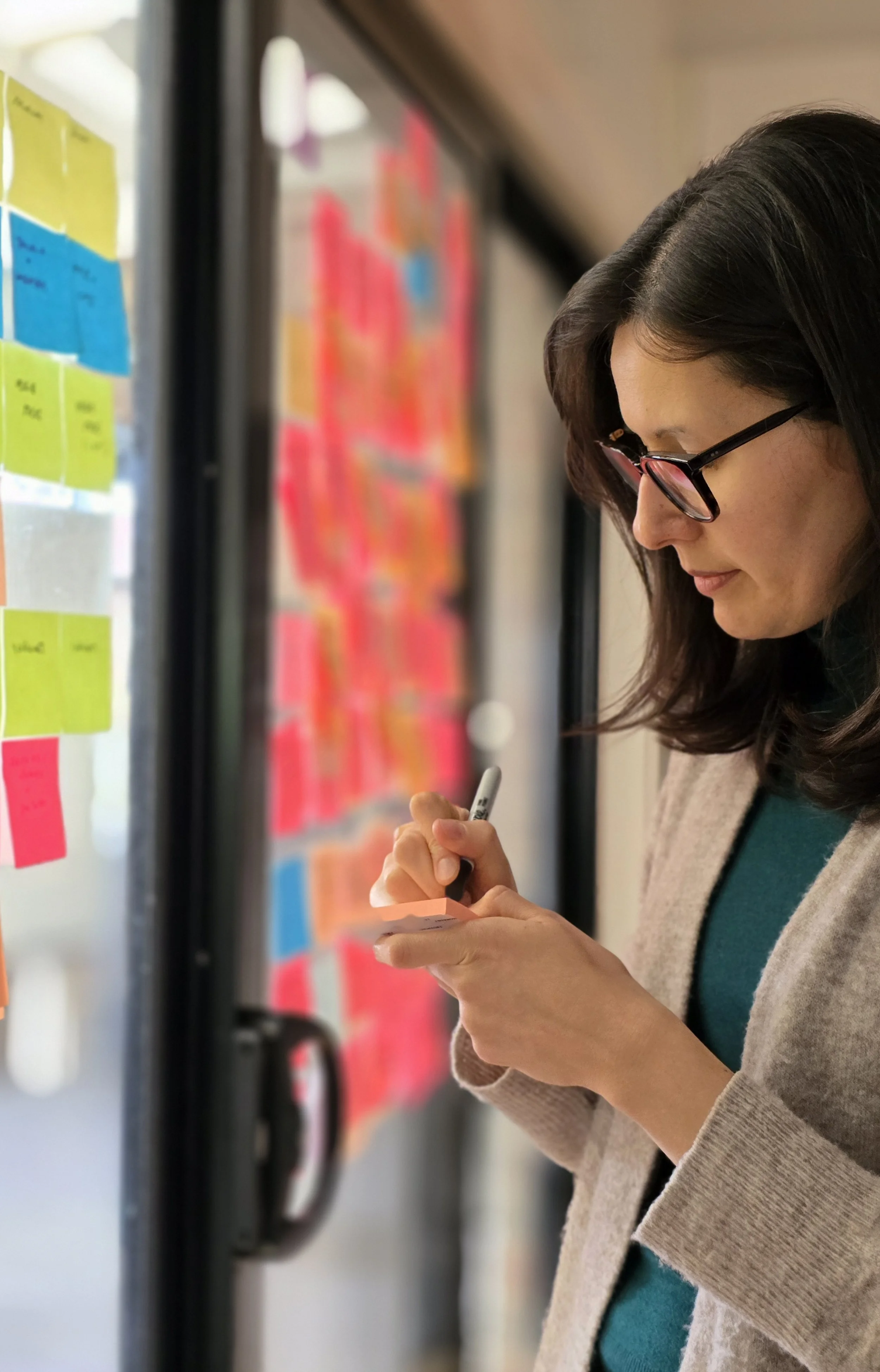 Researcher writing a post it note next to a synthesis wall