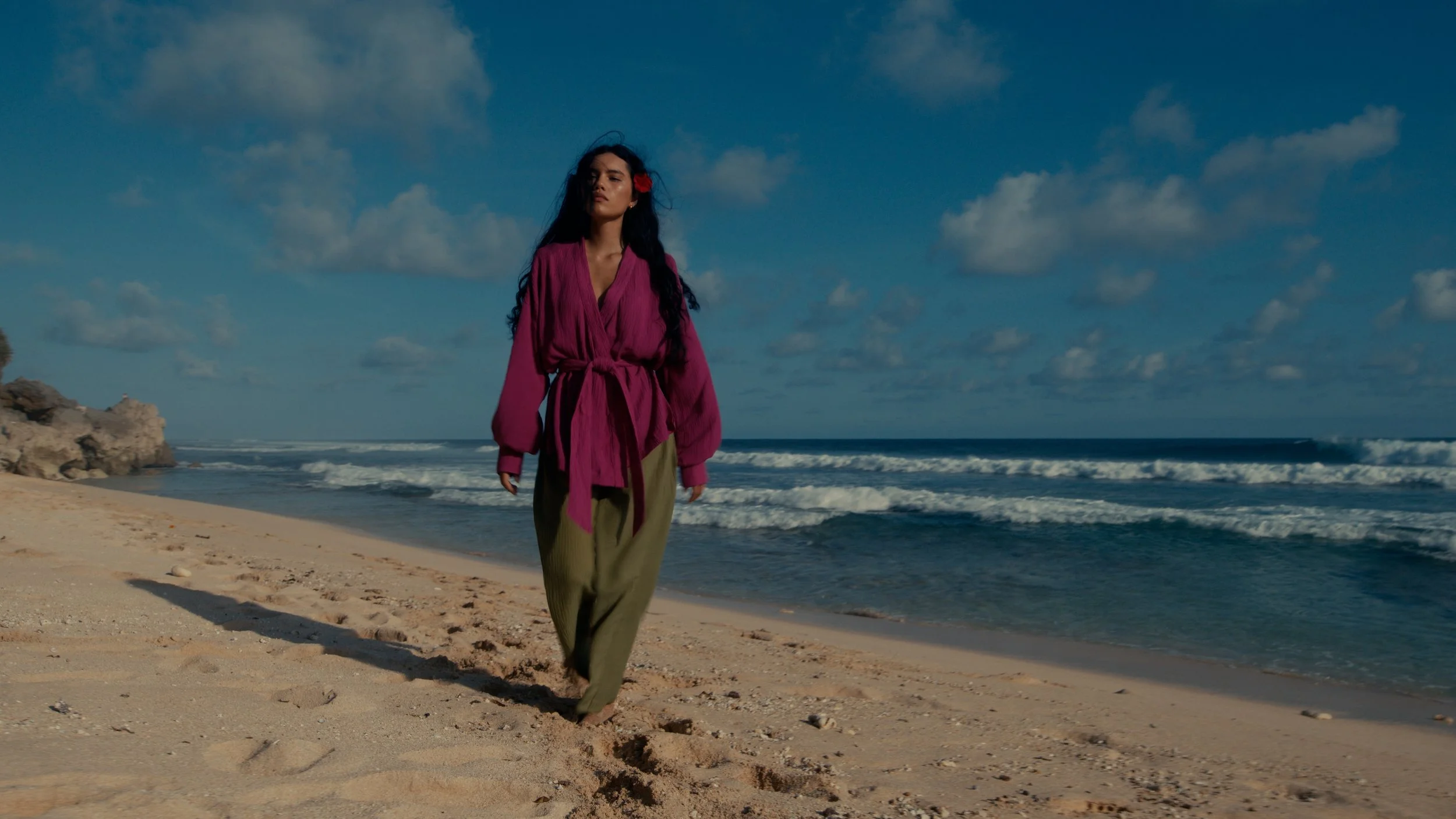 Woman walking on a sandy beach with ocean waves and a partly cloudy sky.