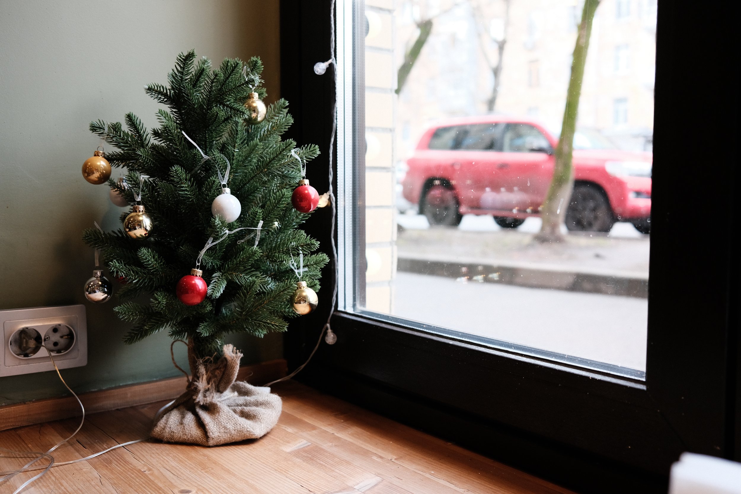 Small decorated Christmas tree near a window with a red vehicle visible outside.