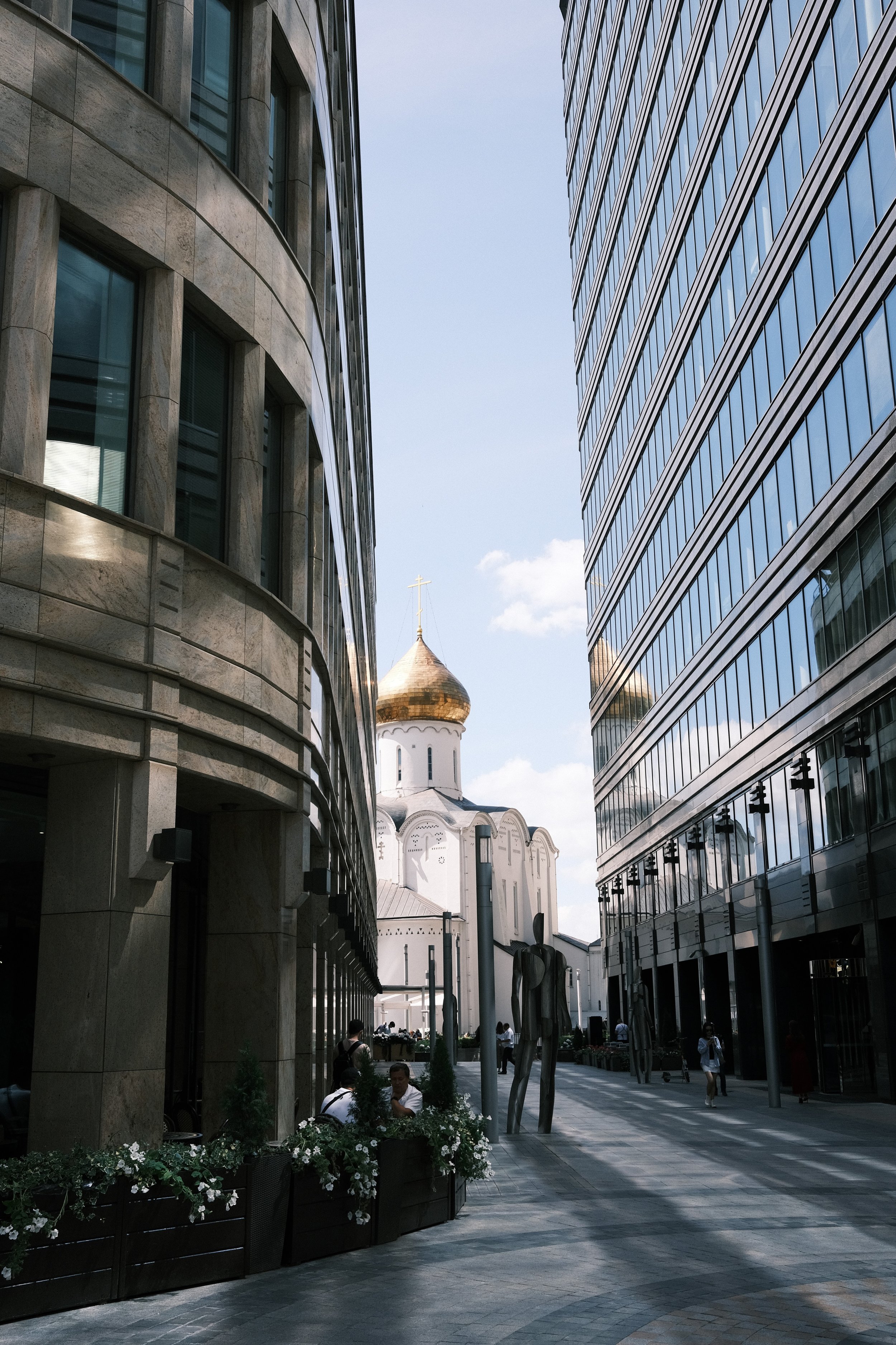 City street with modern glass buildings on both sides and a traditional Orthodox church with golden domes in the background.