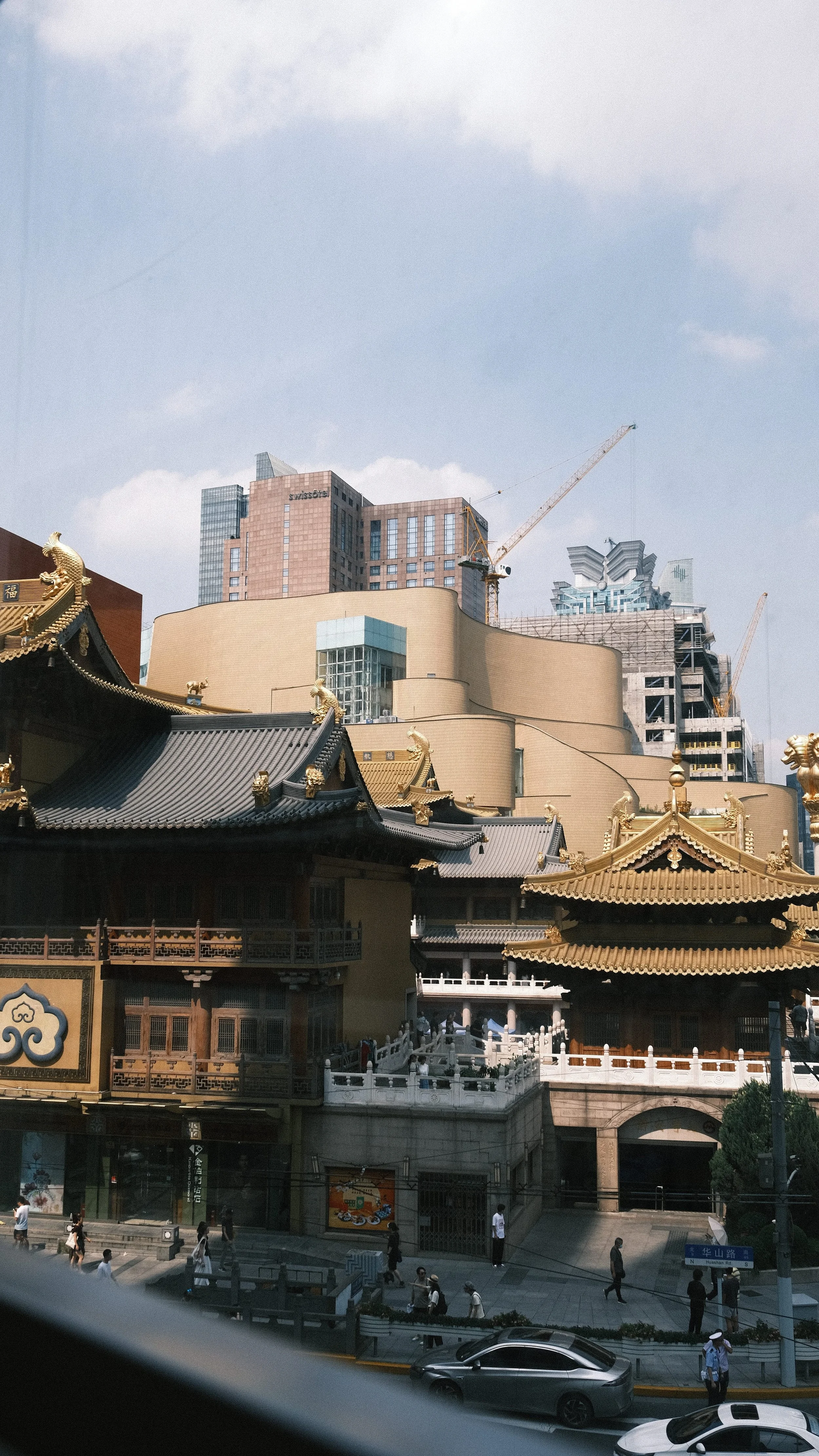 Traditional Chinese temple with ornate rooftops and golden decorations set against modern high-rise buildings under a partly cloudy sky.