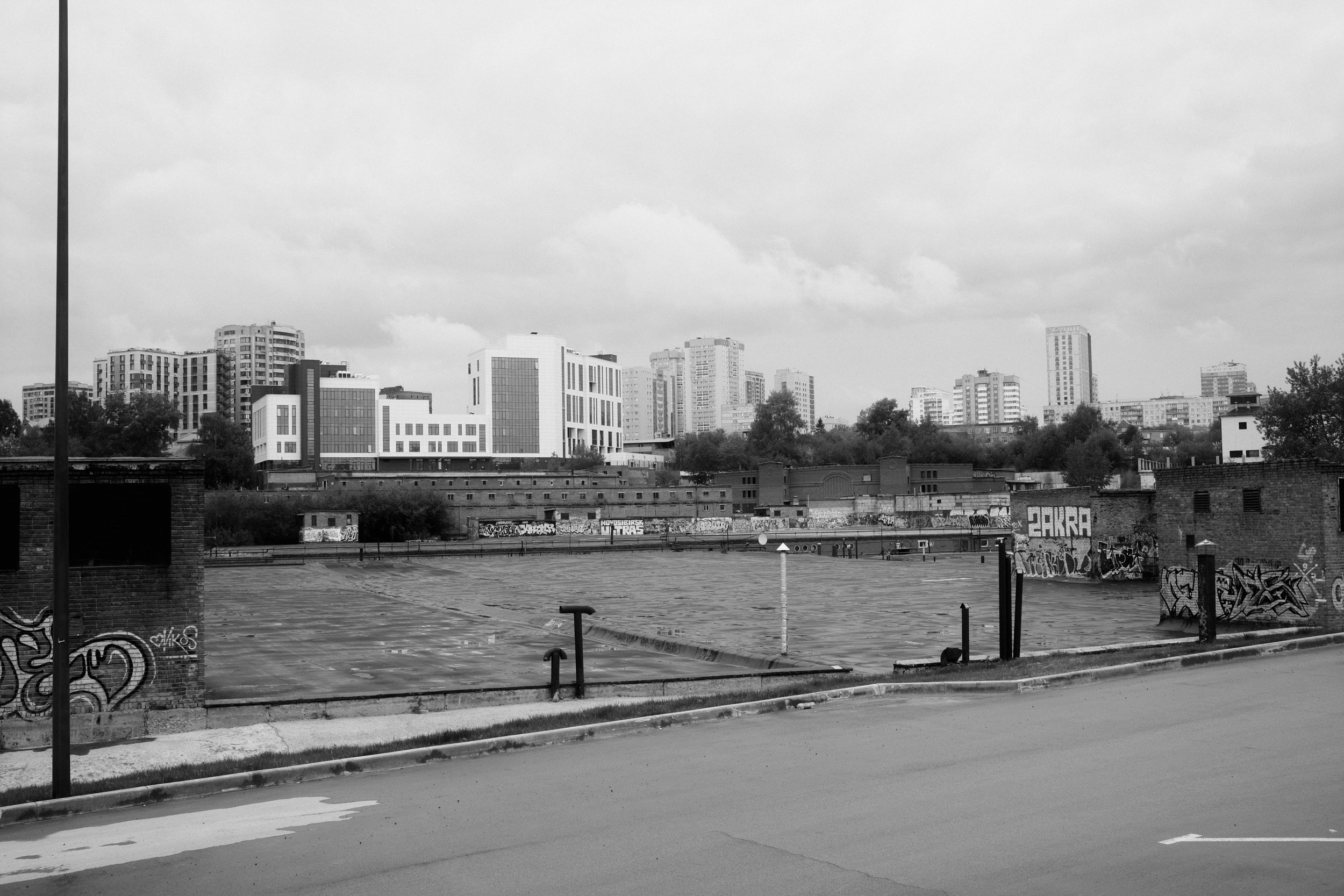 Black and white cityscape featuring a rooftop with graffiti, modern buildings, and cloudy sky.