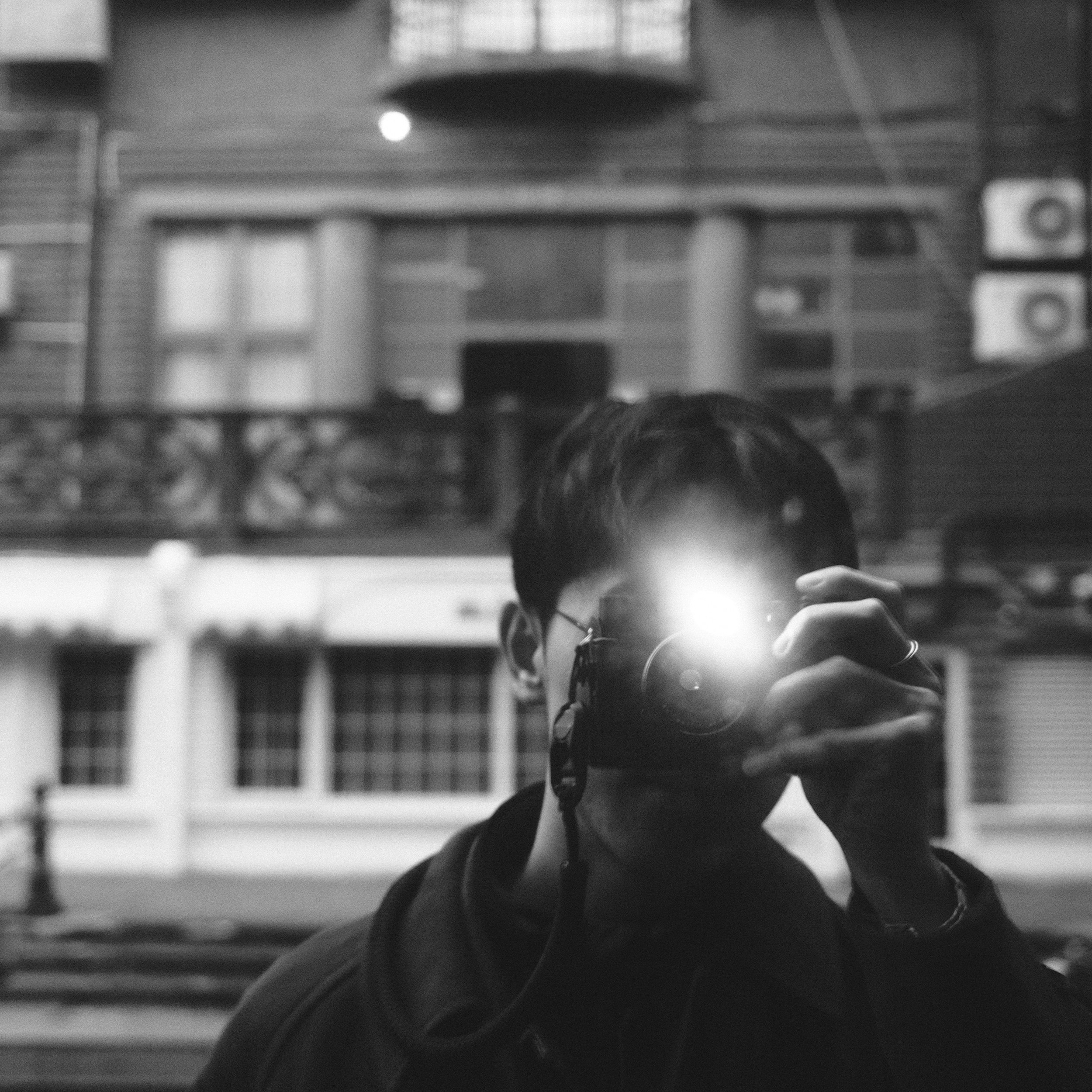 Person taking a photo of themselves in a mirror with a camera flash, urban background visible.