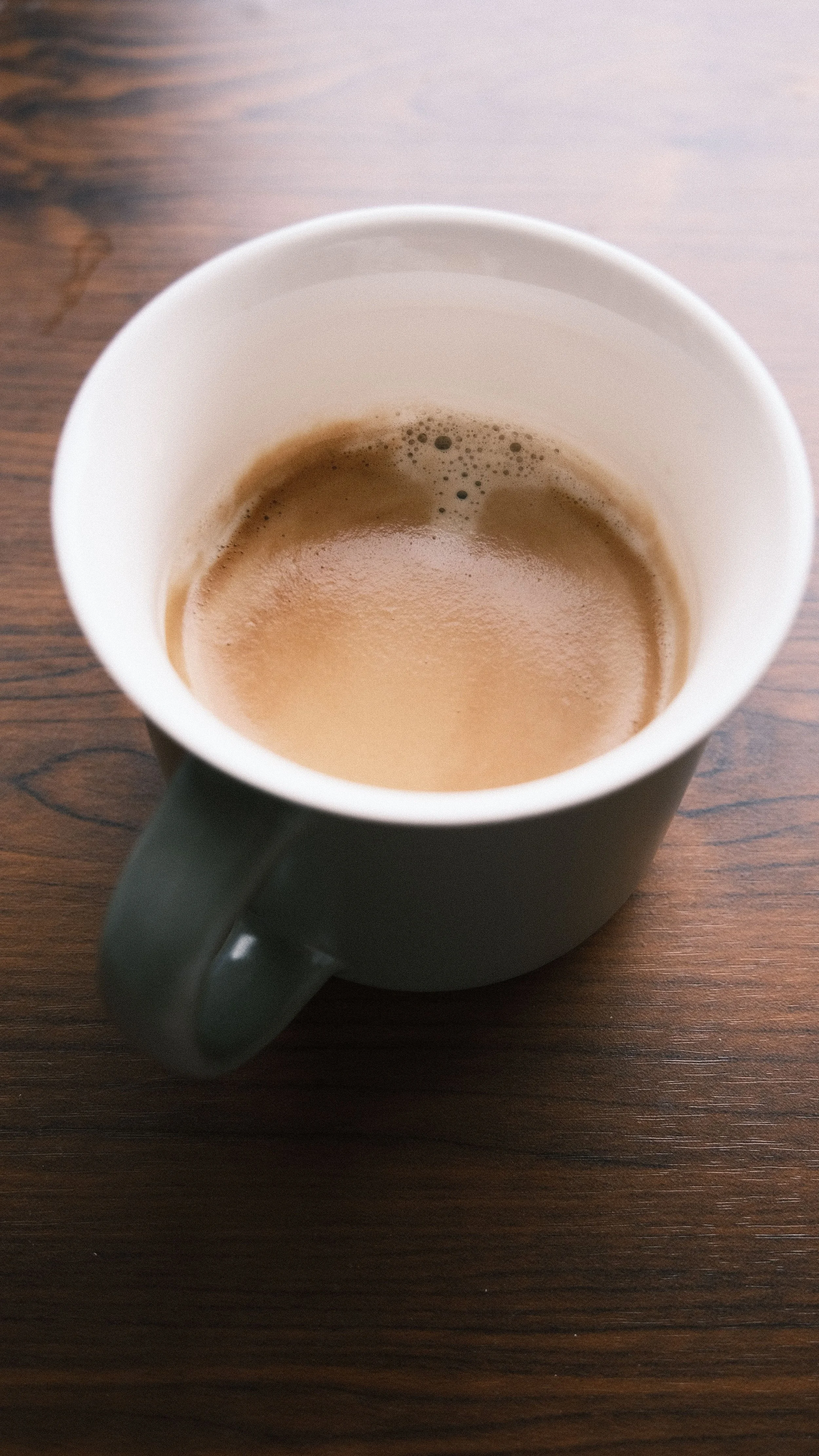 A black ceramic mug filled with hot coffee on a wooden surface.