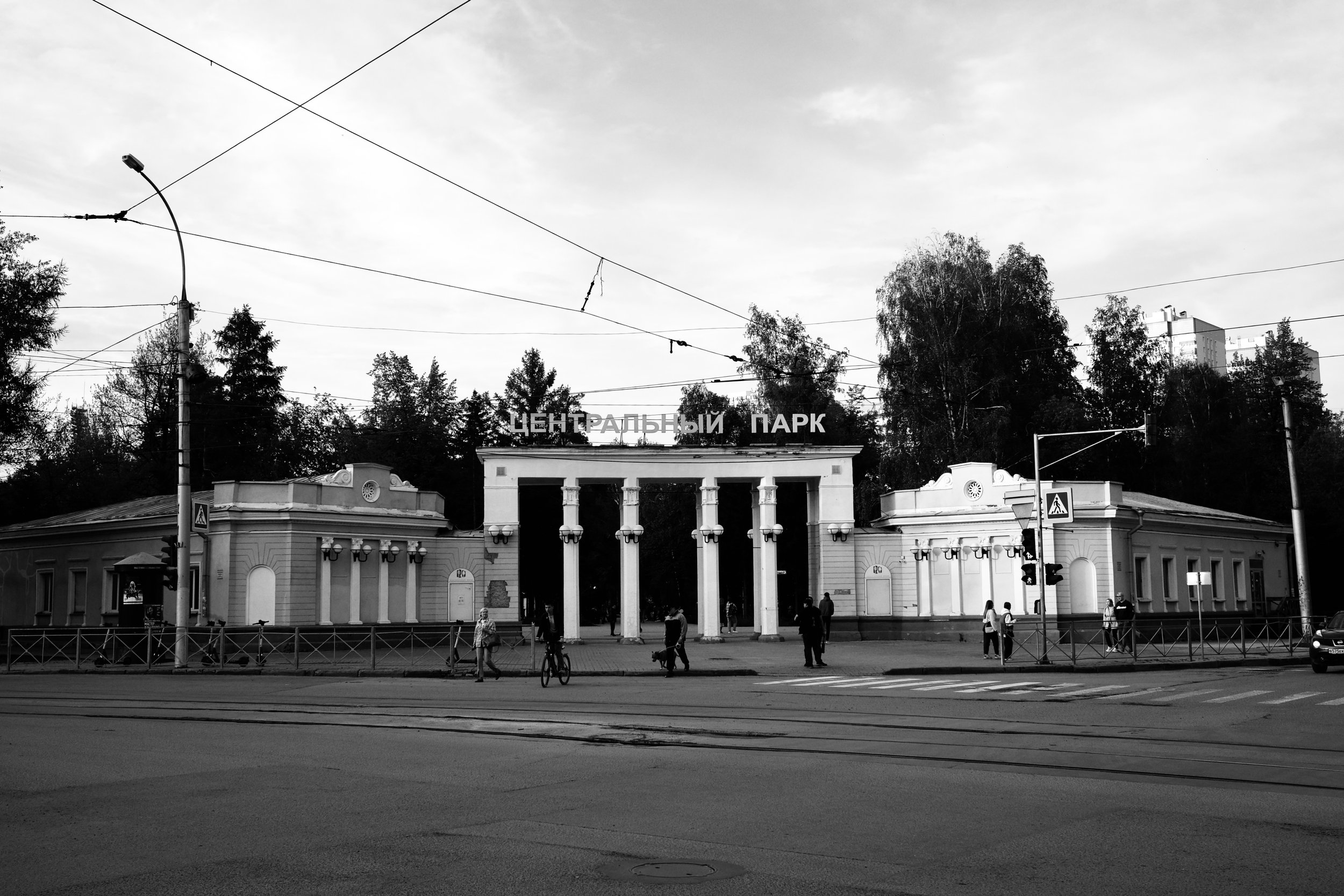 Entrance to Central Park in Russia, with classical architectural gates, people walking, and trees in the background.