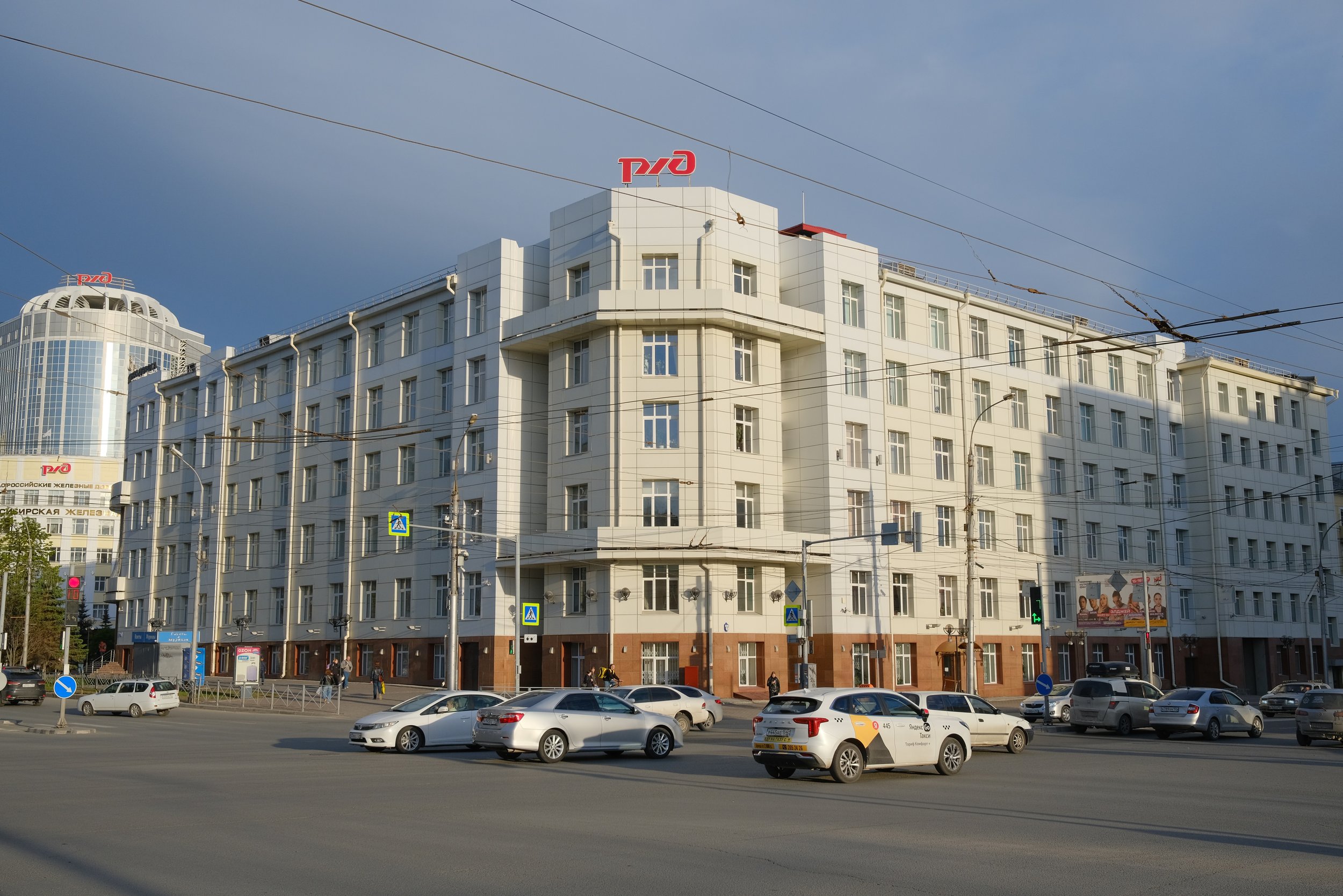 White multi-story building with signage on top, cars parked and driving on street in front.