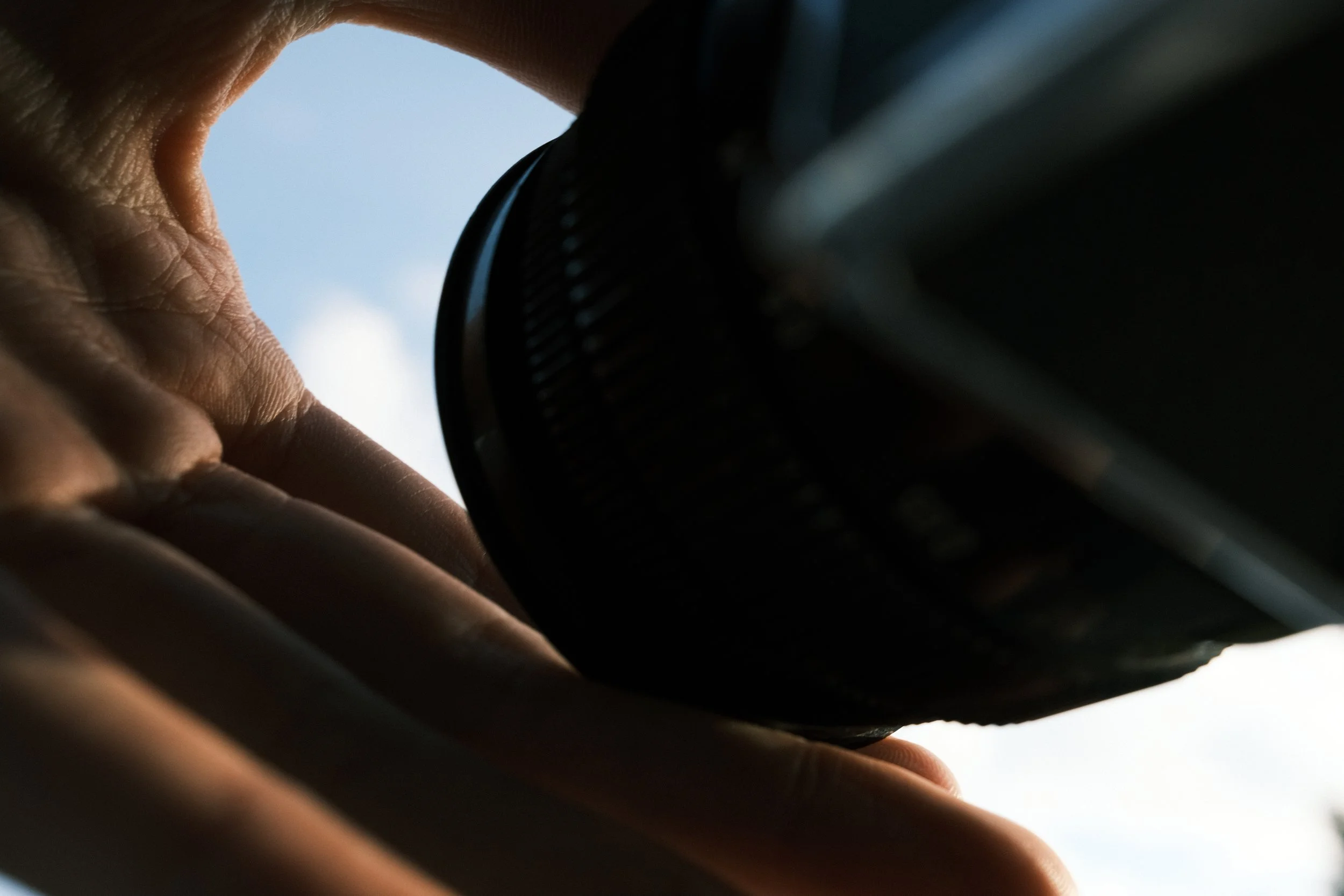Close-up of a person's hand adjusting the focus on a camera lens against a bright sky background.