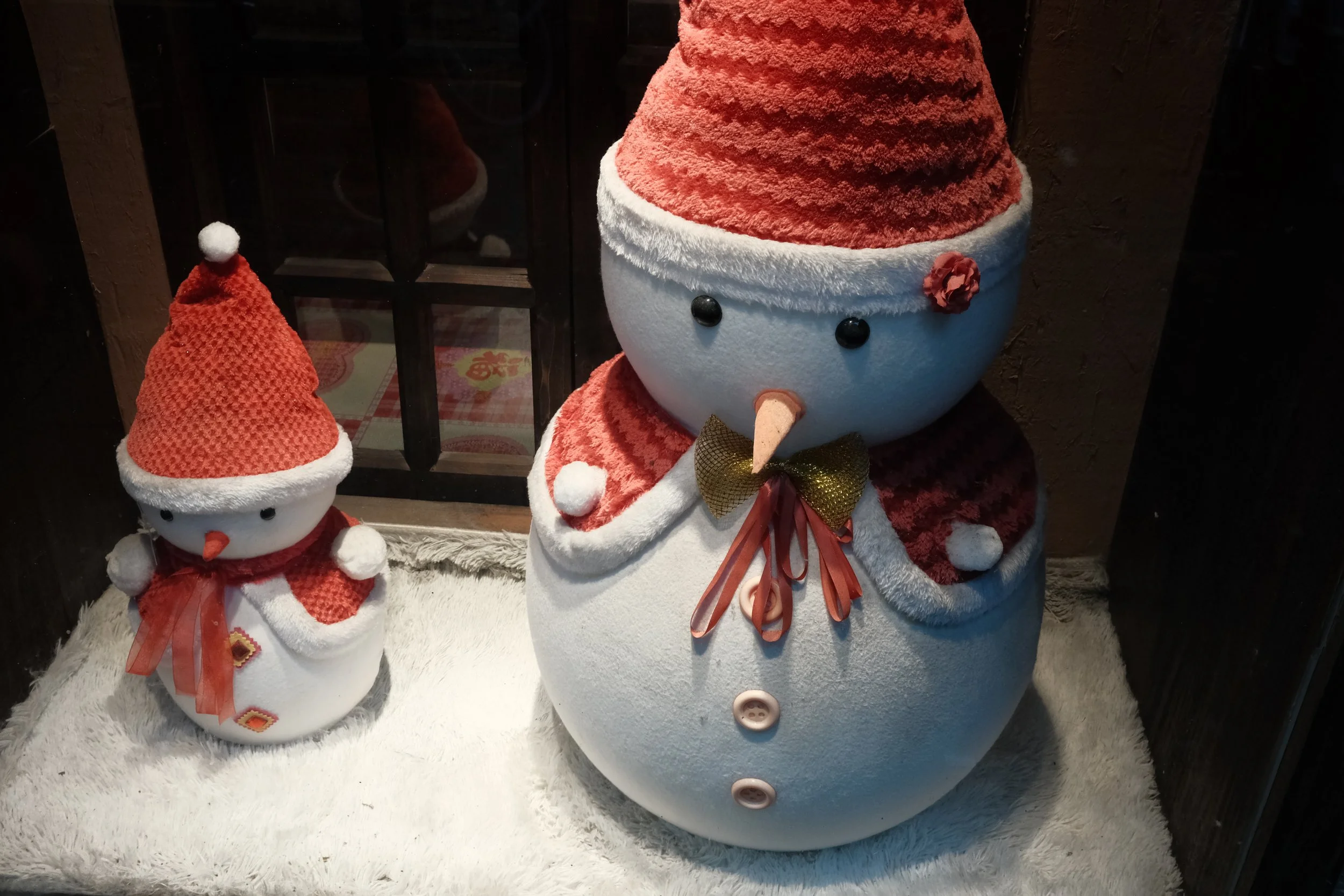 Decorative snowmen with Santa hats and scarves inside a display window.