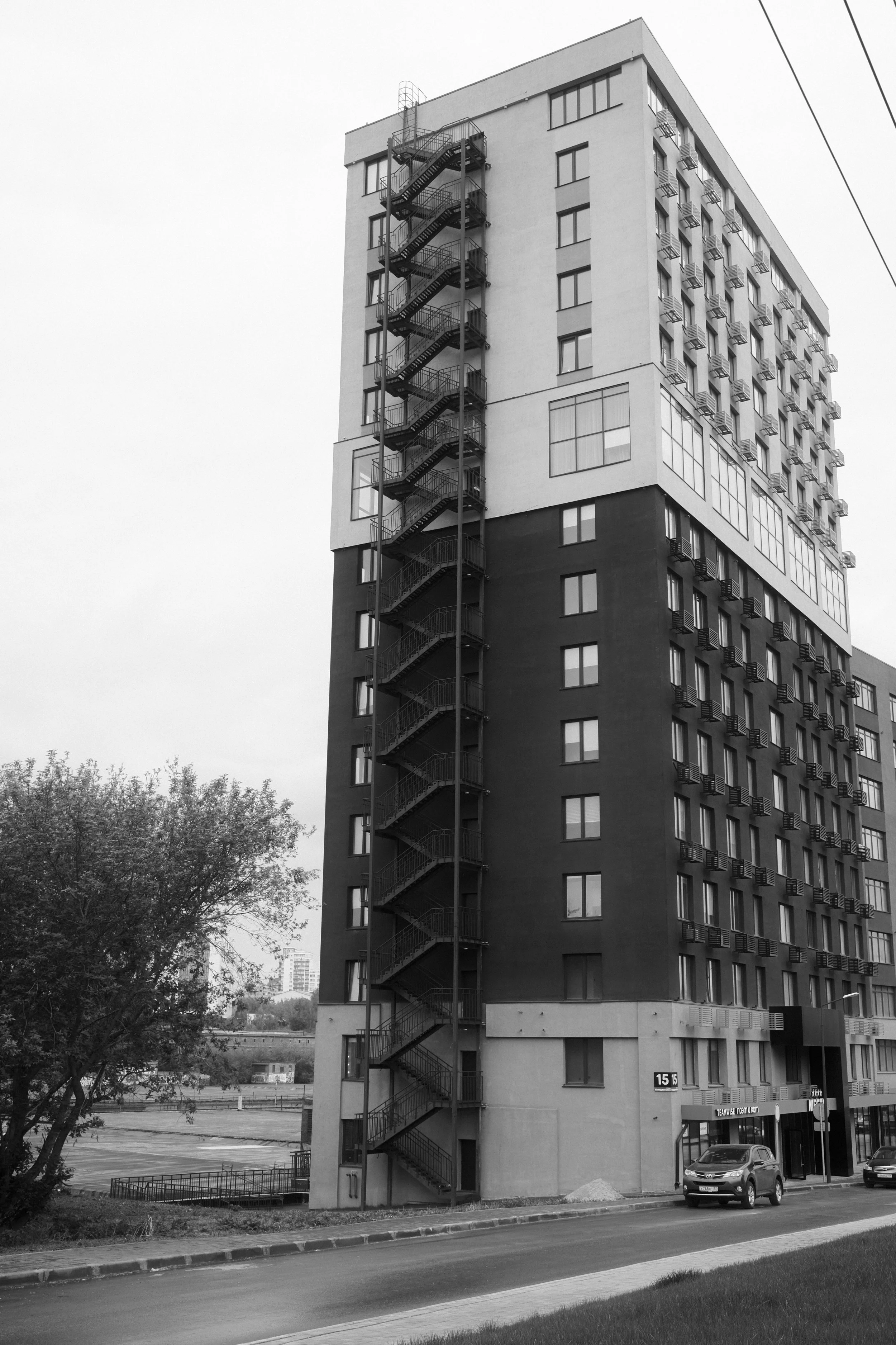 Black and white photo of a multi-story residential building with external fire escape stairs on the side.