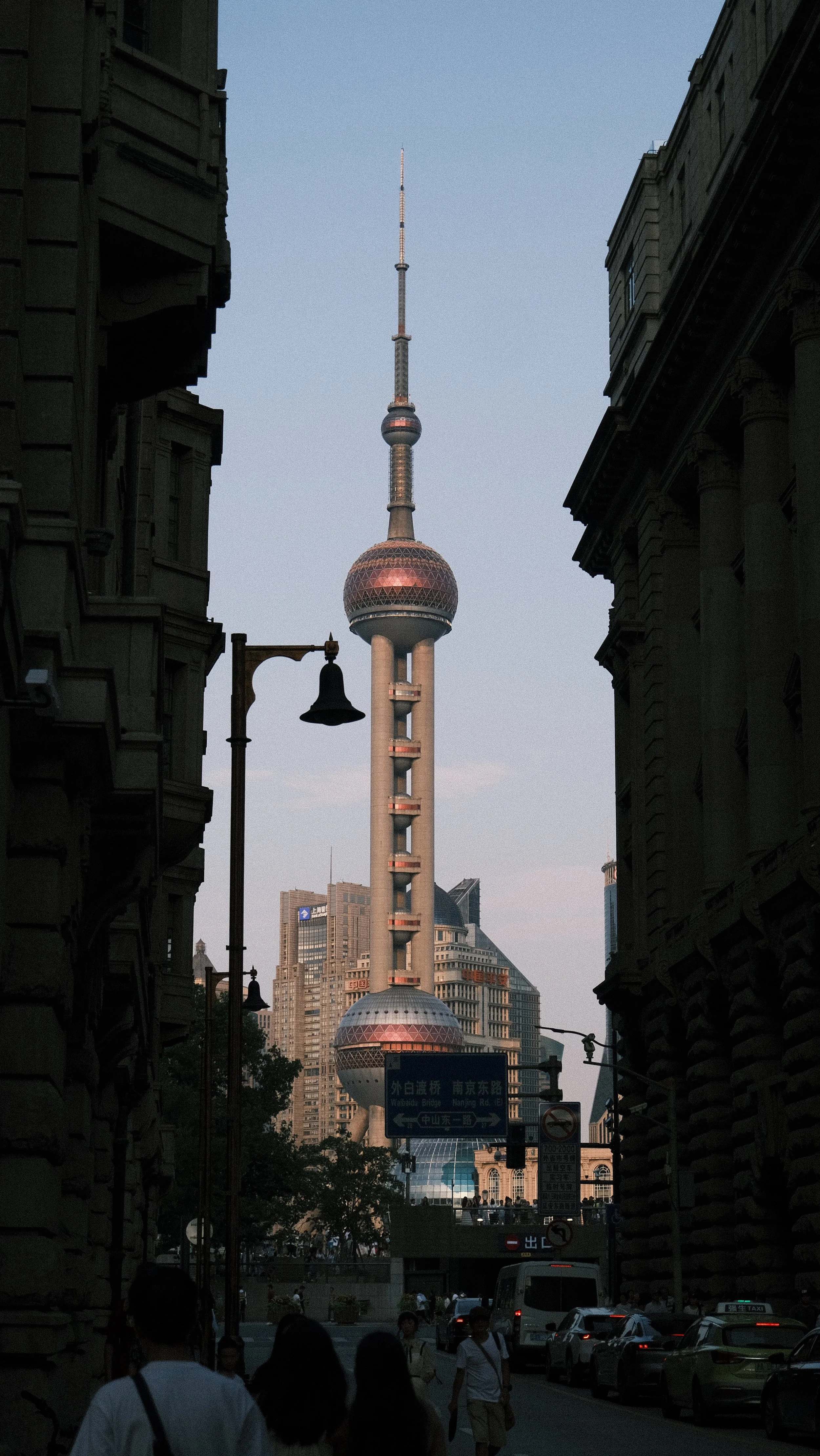 View of the Oriental Pearl Tower in Shanghai framed by dark city buildings and street scene with pedestrians and cars.