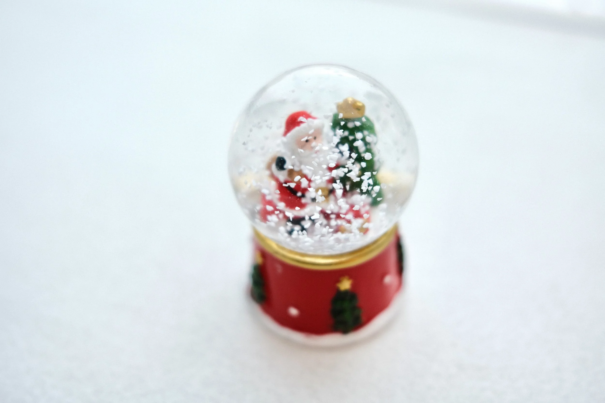 Miniature Christmas snow globe with Santa Claus and a Christmas tree inside, decorated with snow and a red base with Christmas trees.