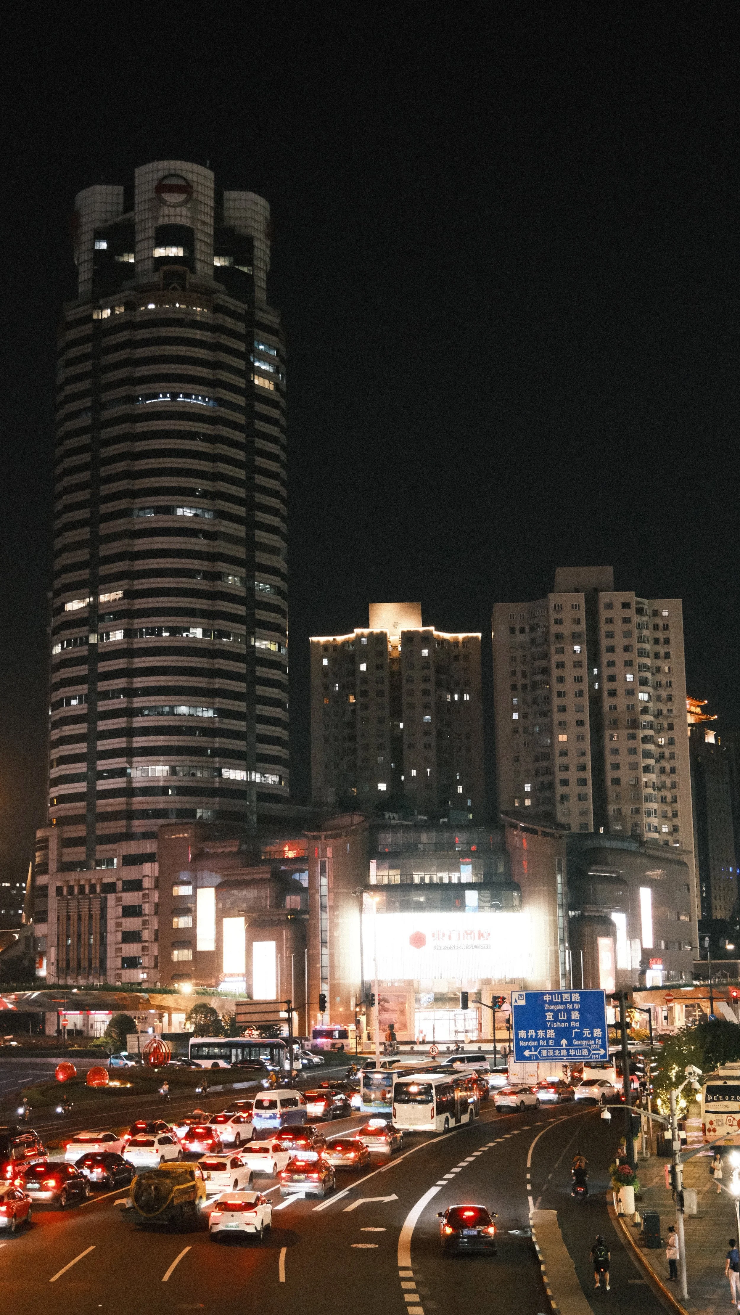 Nighttime city scene with tall buildings, traffic congestion, and illuminated signs.