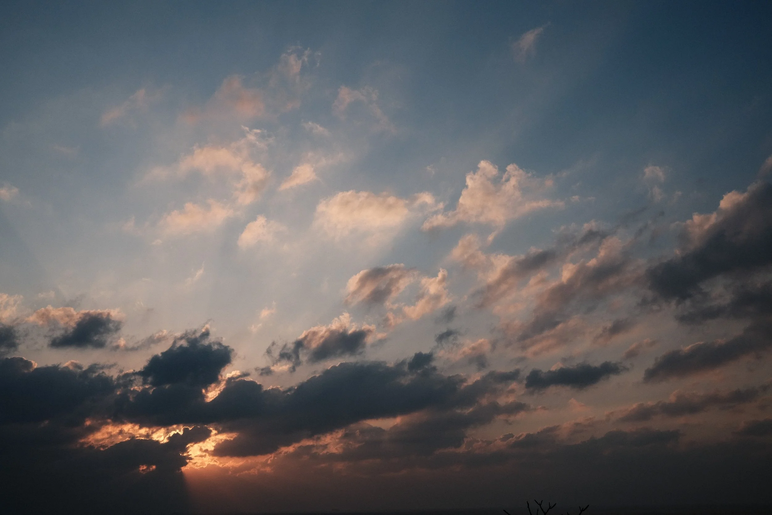 Sunset sky with dark clouds and scattered pink-tinged clouds.