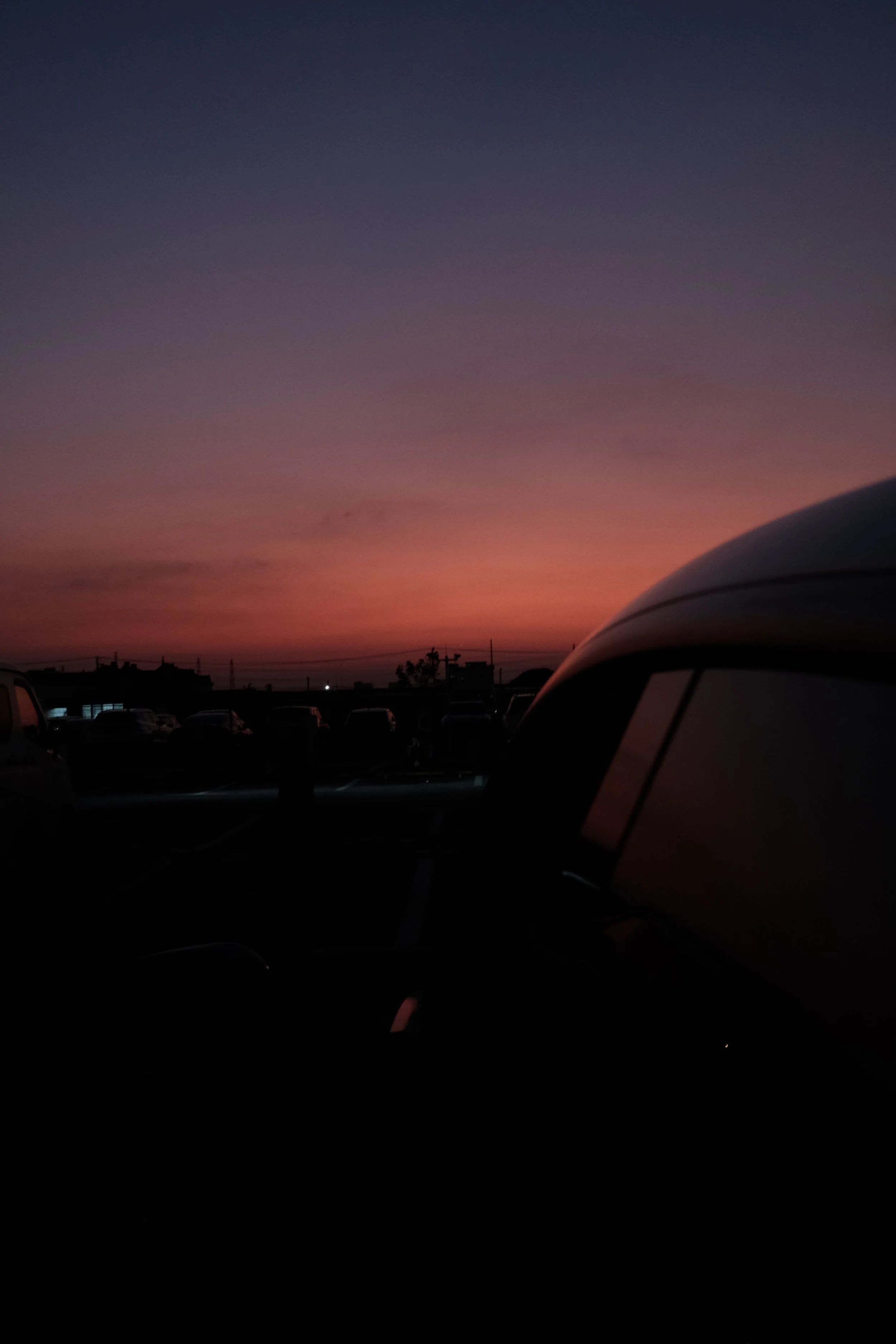 Dusk sky with pink and purple hues, parked cars silhouetted in a lot.