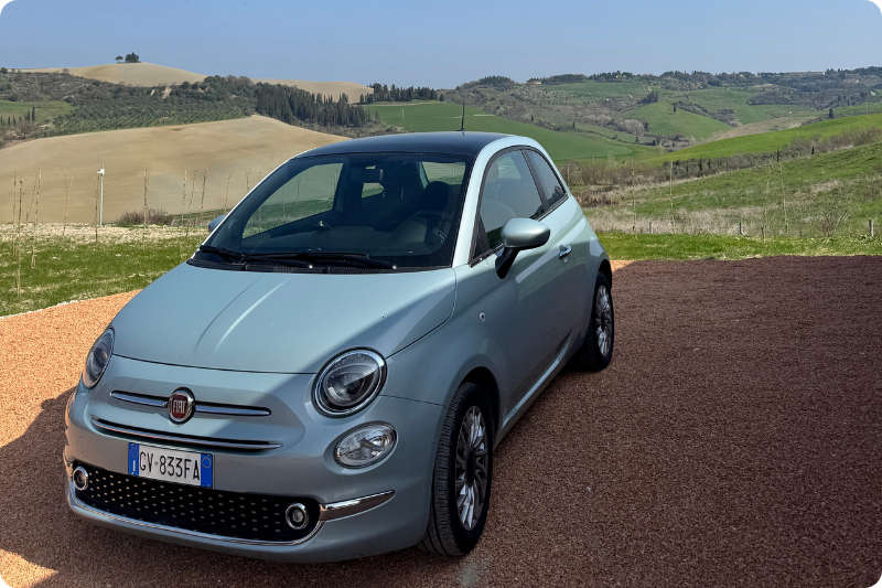 Blue Fiat 500 with Tuscan hills in the background