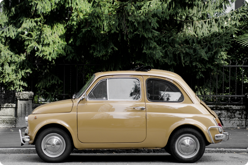 Classic vintage Fiat 500 parked on a quiet Italian street with trees in the background
