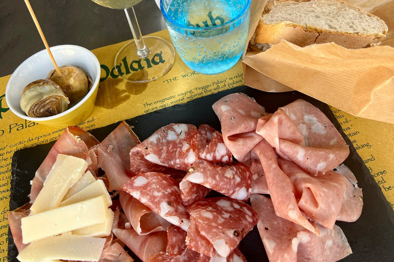 Traditional Tuscan lunch with cured meats, cheeses, bread, and marinated onions served on a table with wine and water, capturing authentic Italian food and local dining experience in Tuscany