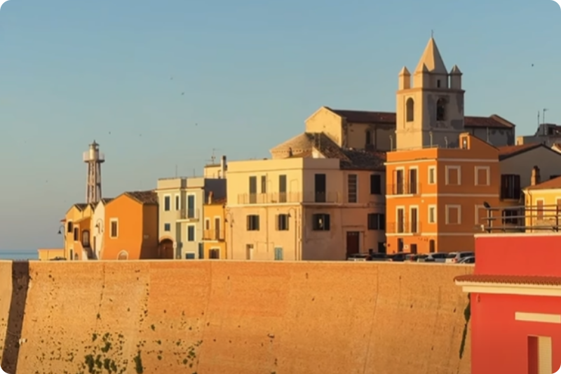 Sunlit coastal Italian town with pastel-coloured buildings, church tower and lighthouse overlooking the sea, capturing the charm of hidden seaside destinations and slow travel in Italy.