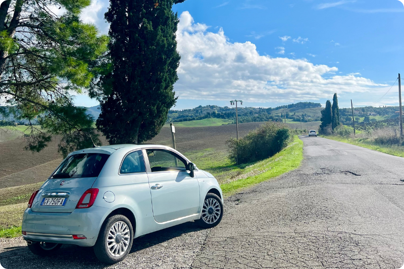 Light blue Fiat 500 rental car parked at the side of the road in Tuscany..