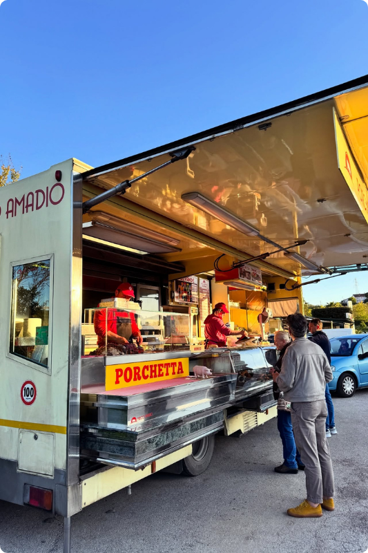Traditional Italian street food truck serving fresh porchetta at sunset, with local customers gathered outside, showcasing authentic regional food culture and everyday culinary experiences in Italy.