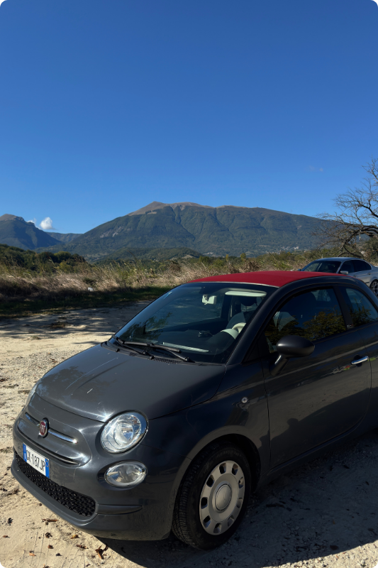 Black Fiat 500 parked with Tuscan hills in the background