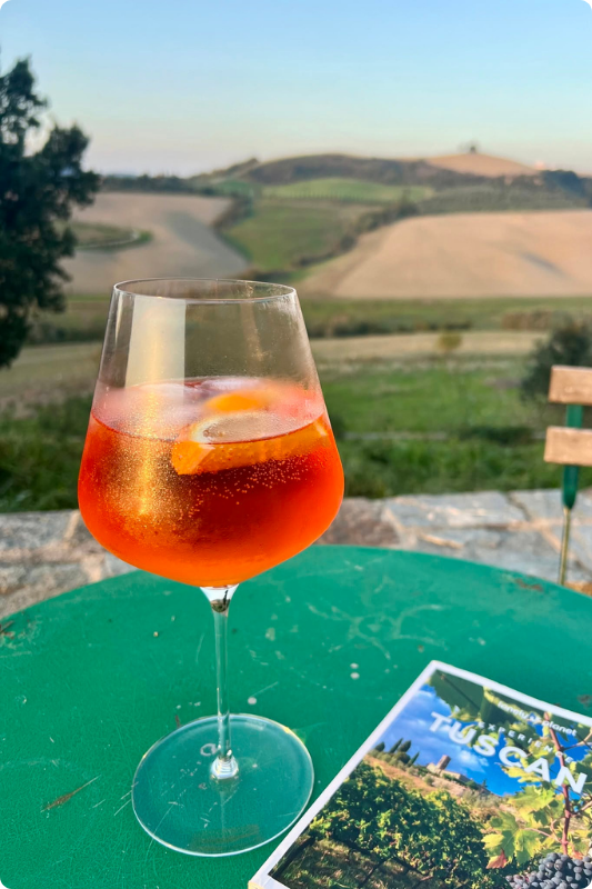 A glass of Aperol Spritz with the Tuscan sunset in the background
