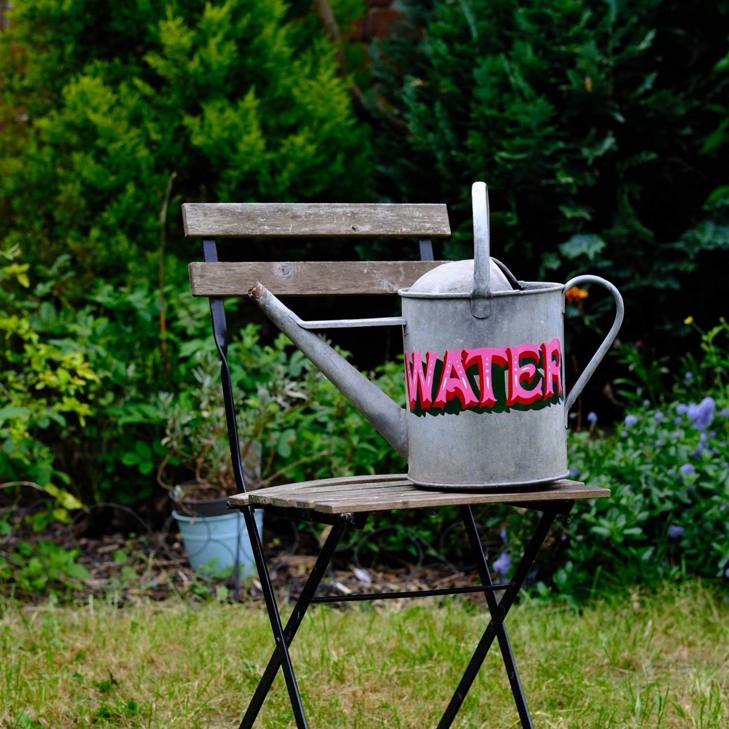 Vintage tin watering can, hand painted with modern carnival style hand lettering reading WATER in pink and red