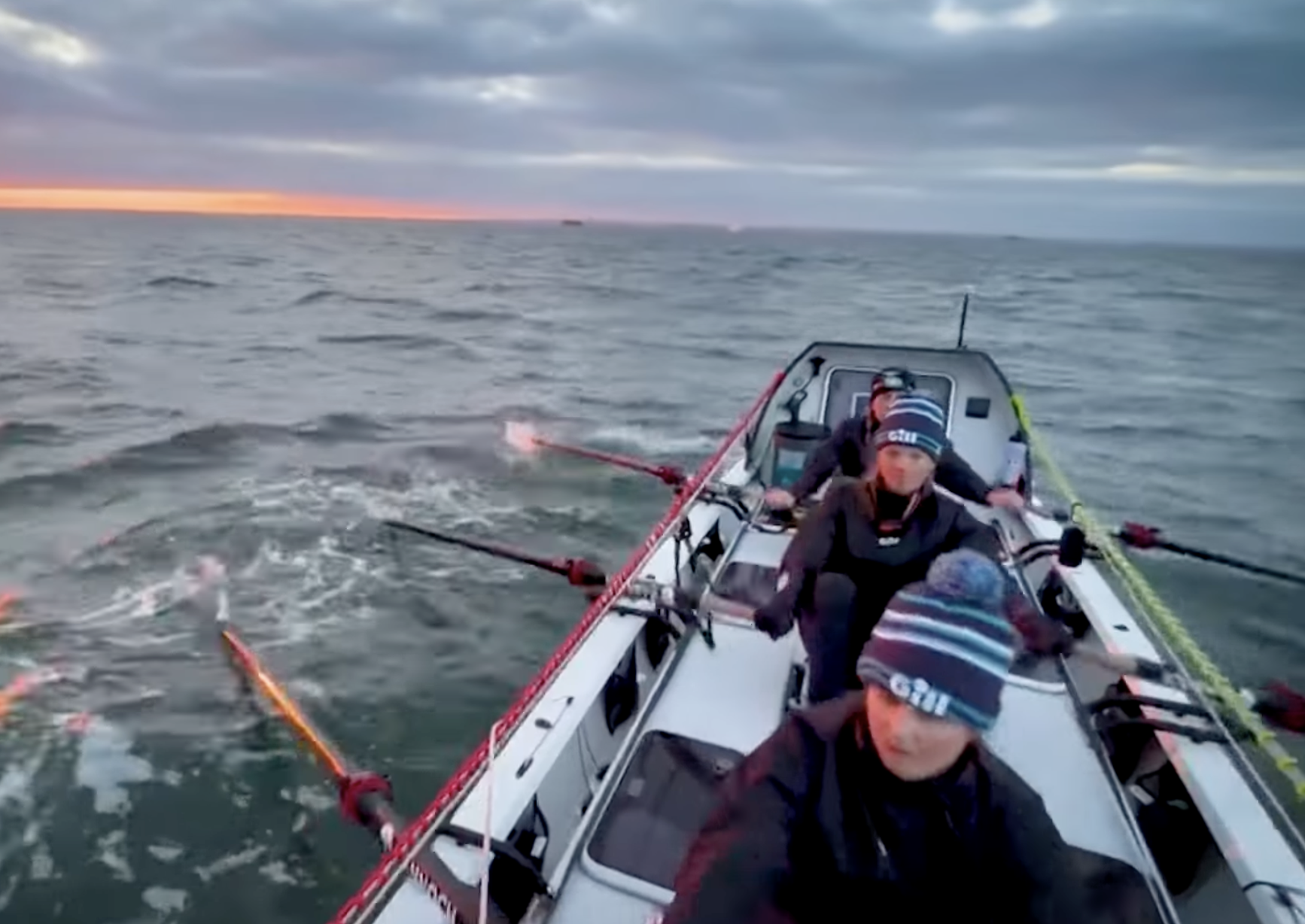 People rowing a boat on the ocean during sunset, with cloudy sky.