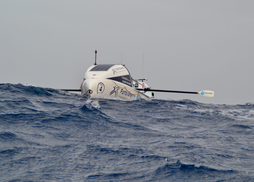 A sleek white autonomous underwater vehicle (UUV) floating on the ocean surface with waves in the foreground and a gray sky above.