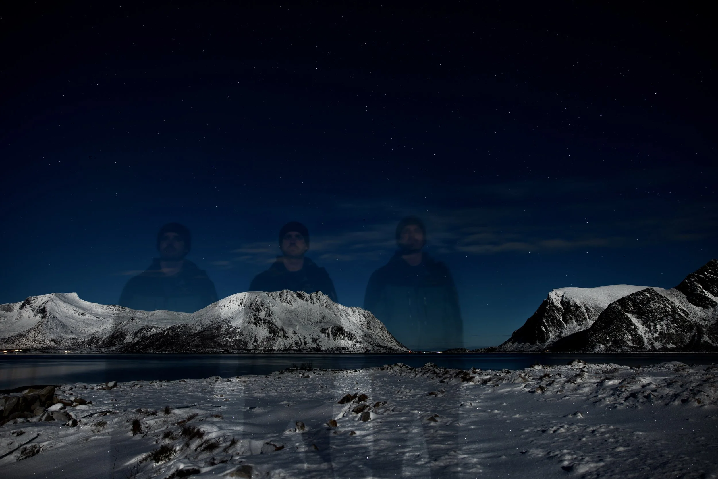 Snow-covered mountains at night with a clear starry sky and a faint reflection of three people walking on snowy ground