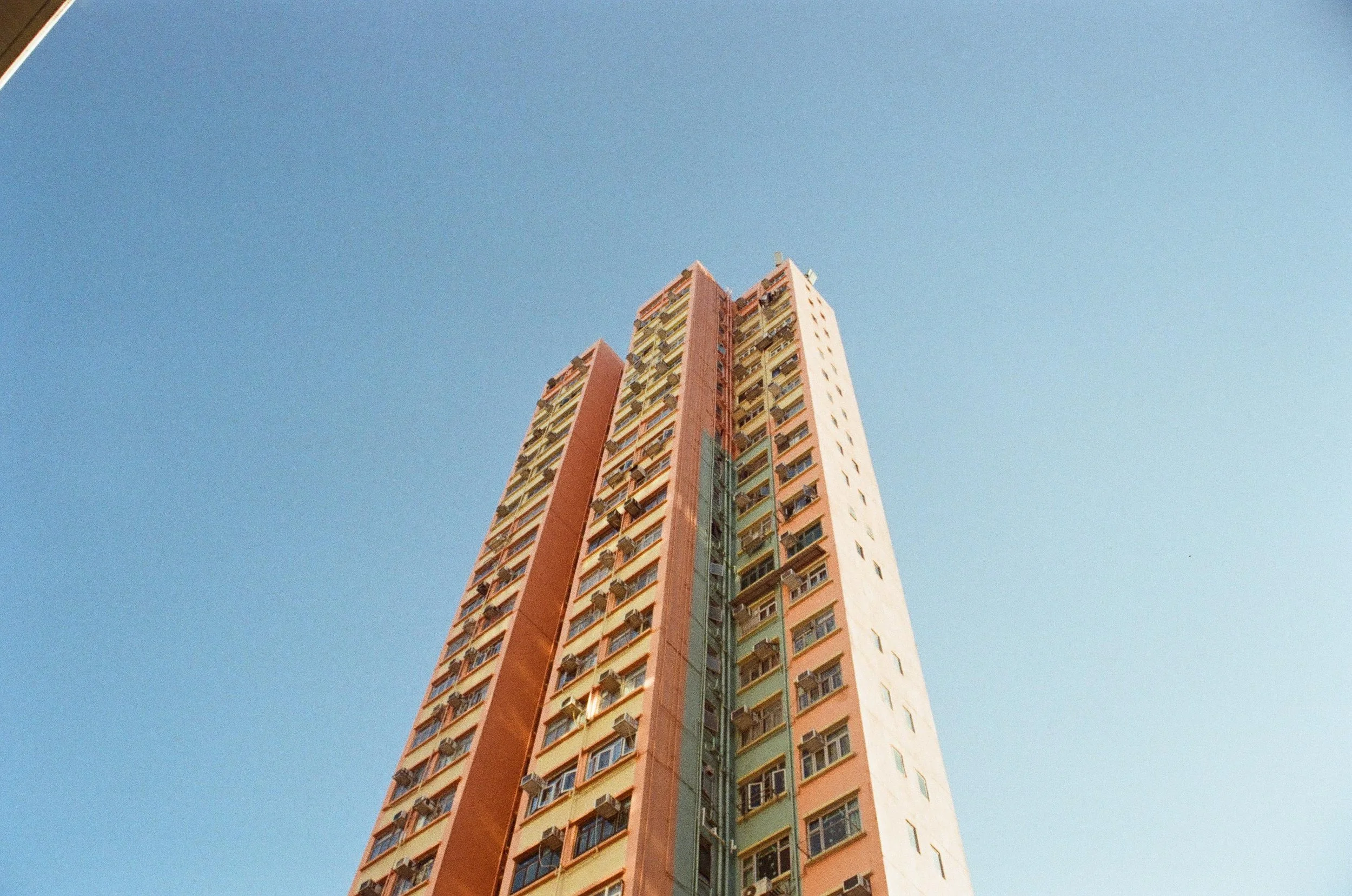 Tall residential apartment building with multiple windows and air conditioning units, against a clear blue sky.