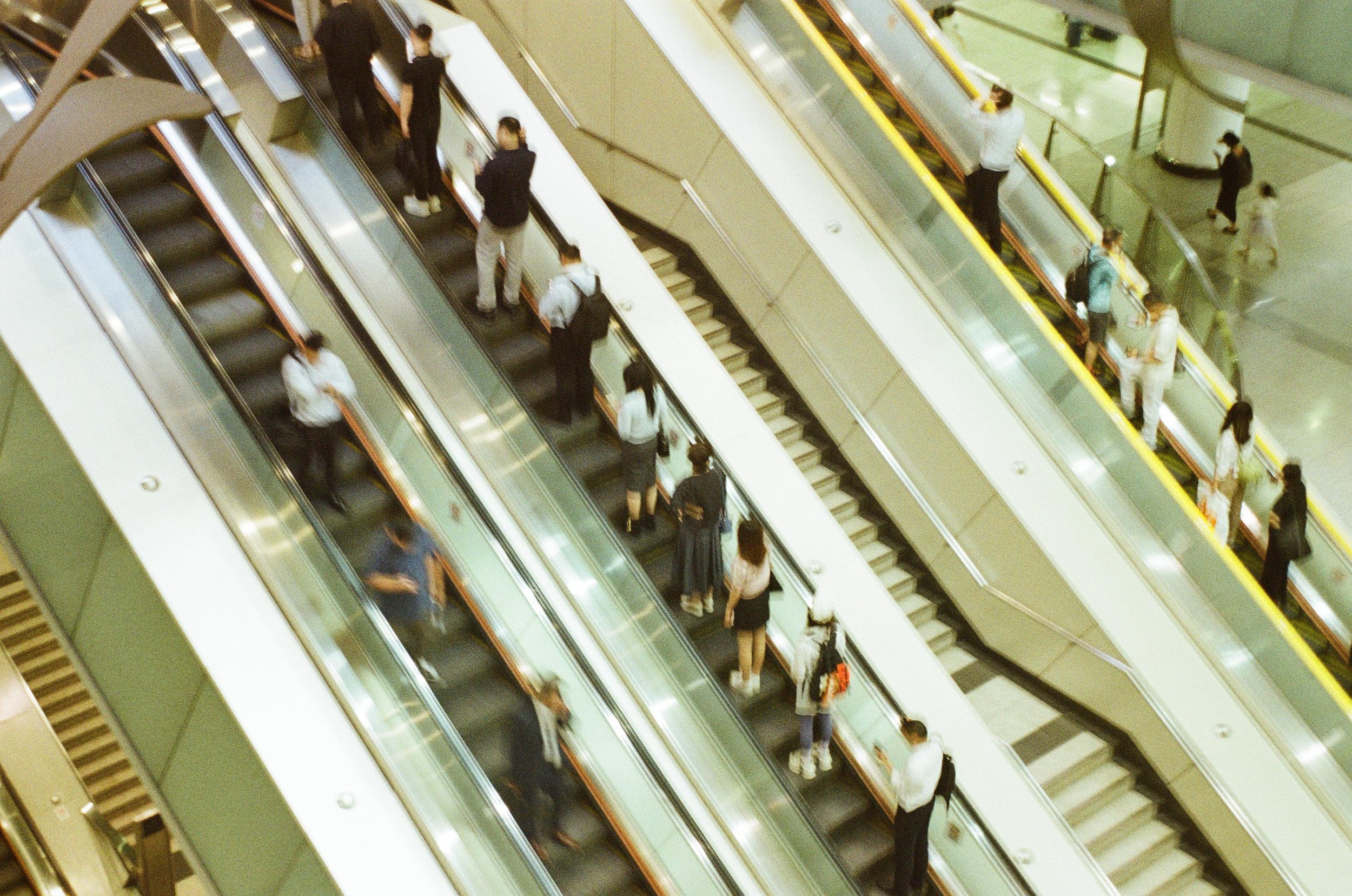People using escalators in a shopping mall or airport, viewed from above.