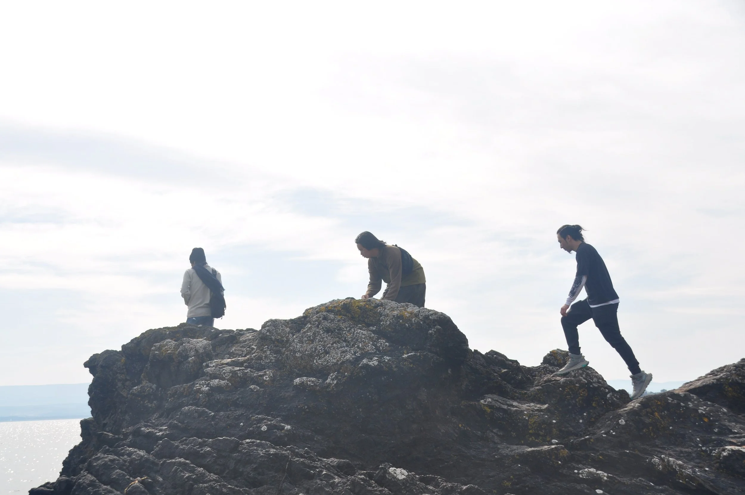 Three people exploring rocks on a coastline.