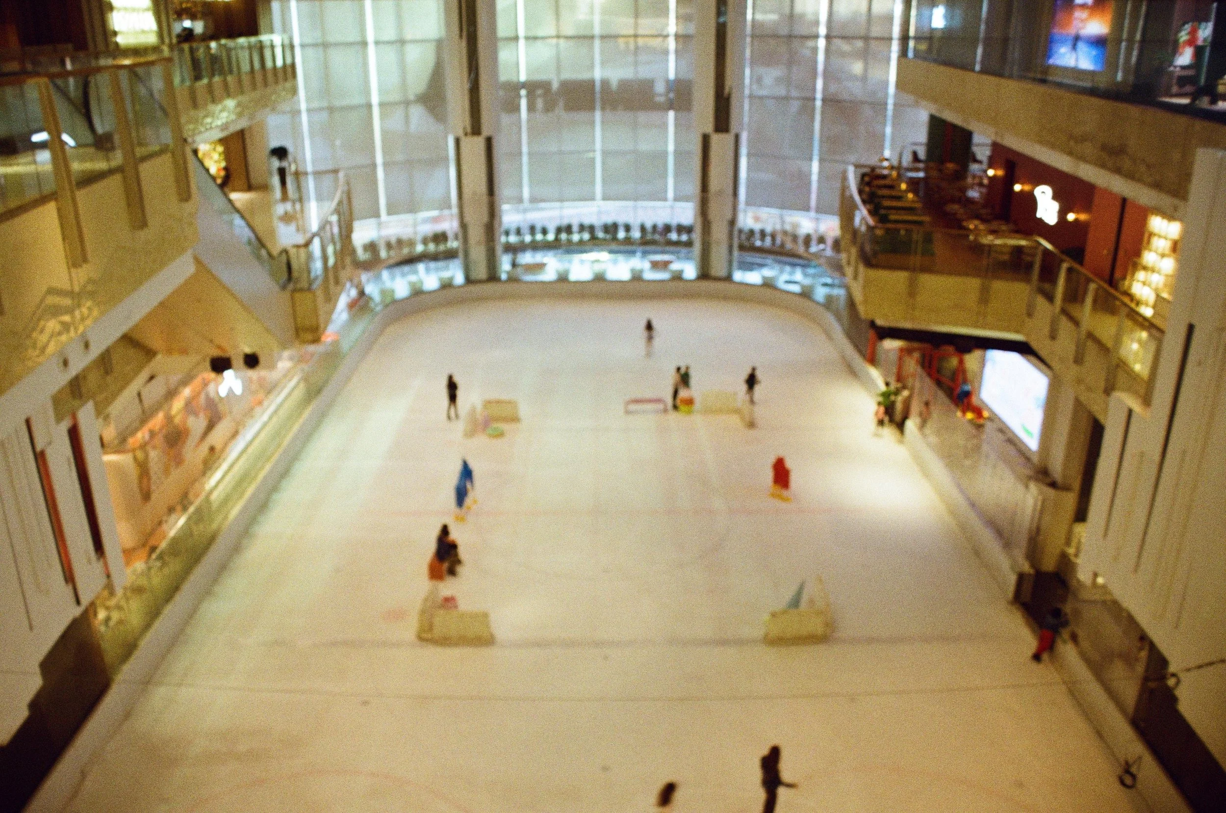 Indoor ice skating rink with several skaters and seating area around it.