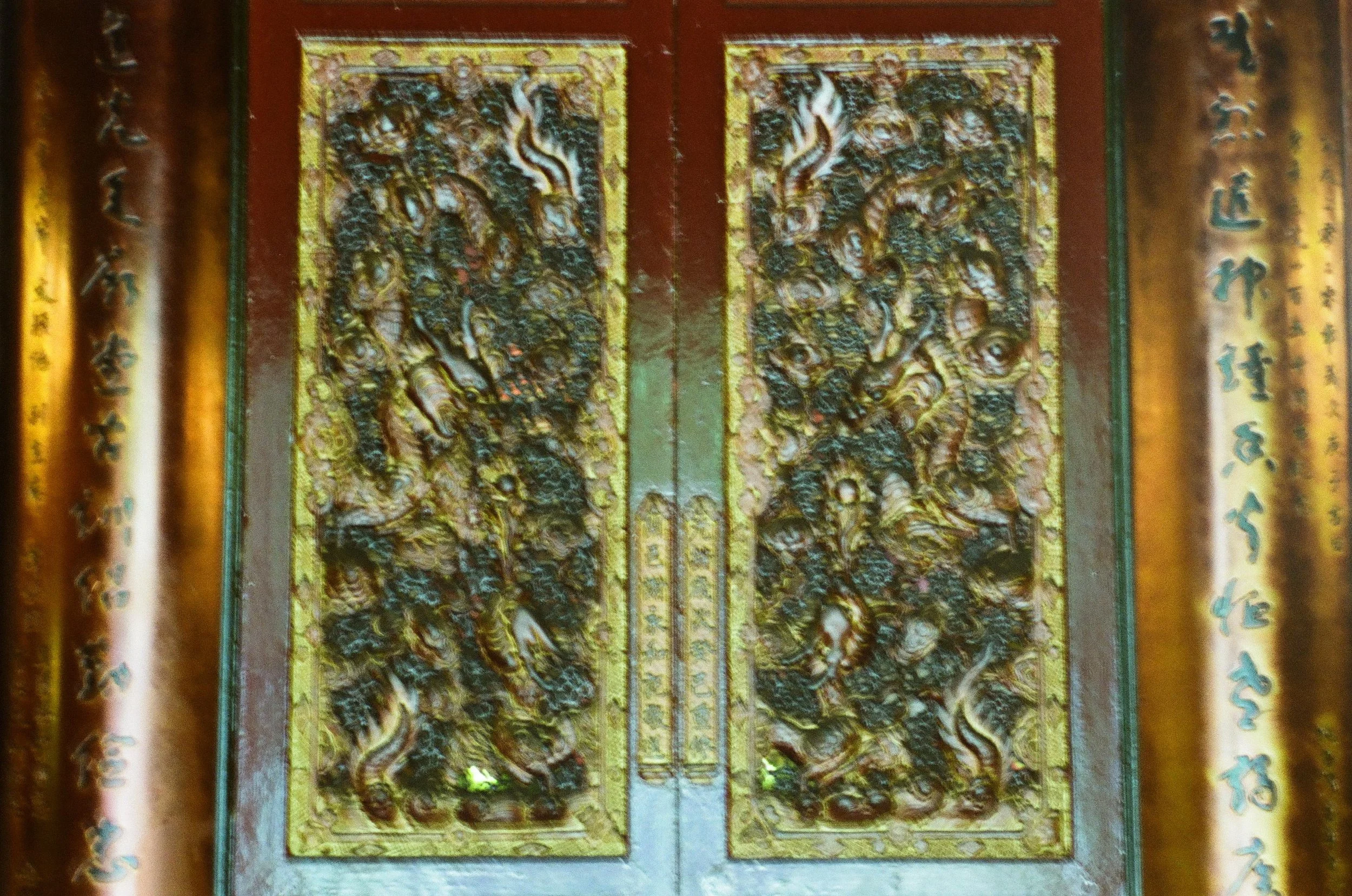 A pair of ornate, golden, carved wooden doors with intricate dragon designs, surrounded by vertical wooden panels with Chinese characters.