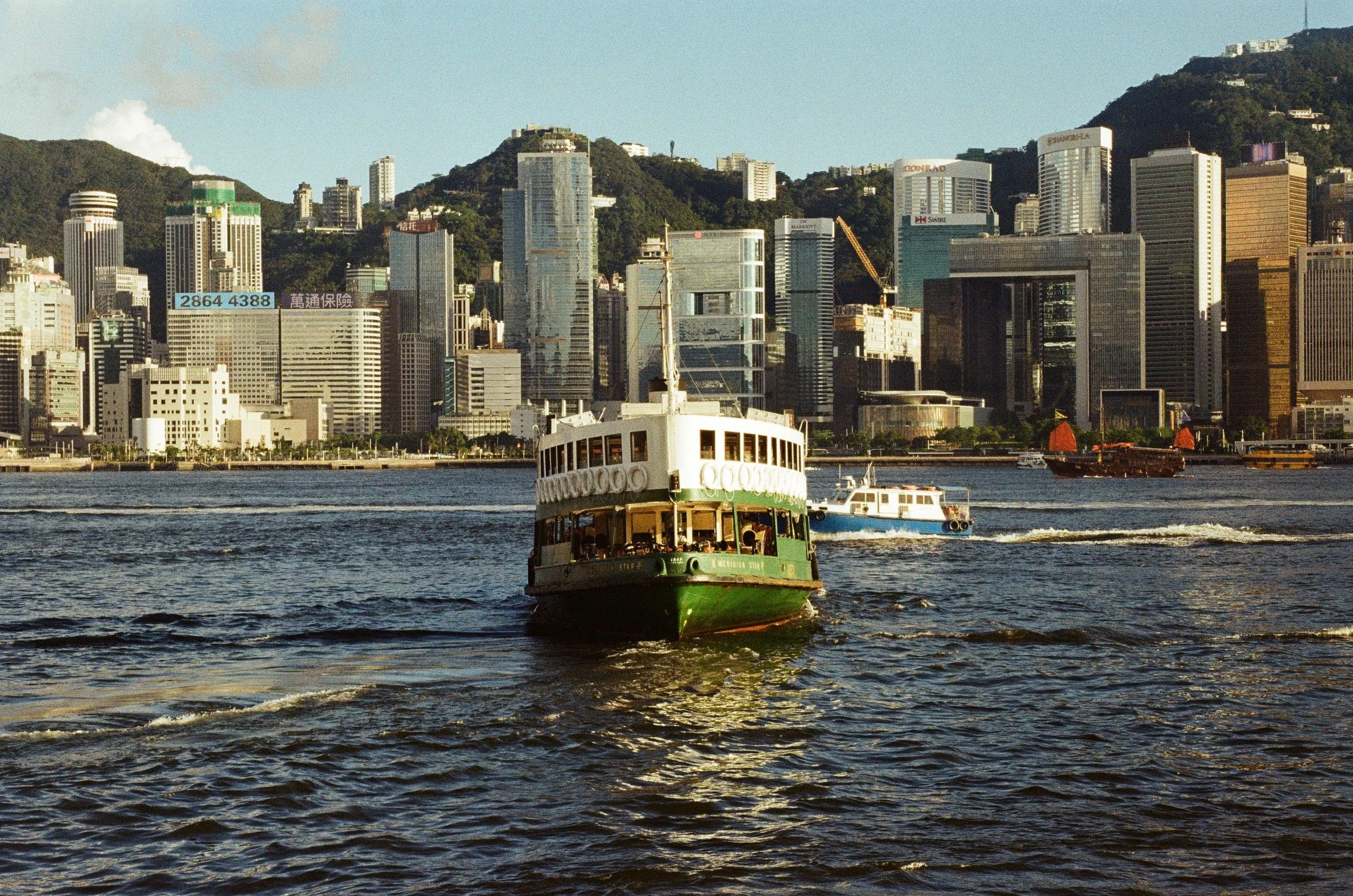 A ferry boat sailing on the water with a city skyline and hills in the background.