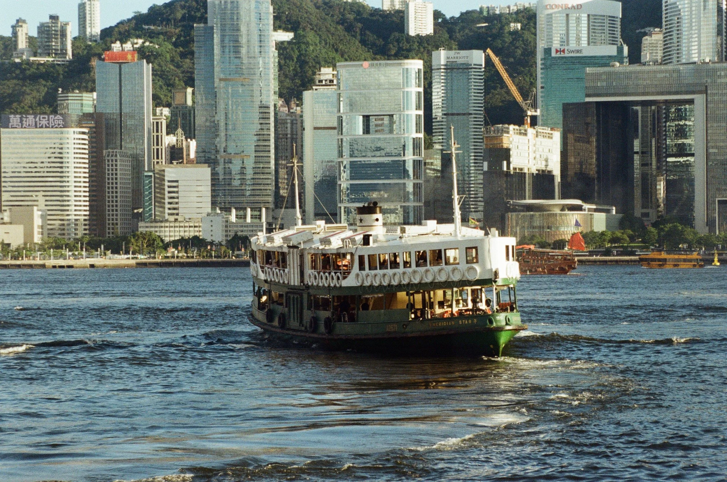 A vintage ferry boat named serverdian star on the water in front of a modern city skyline with high-rise buildings and a hillside in the background.