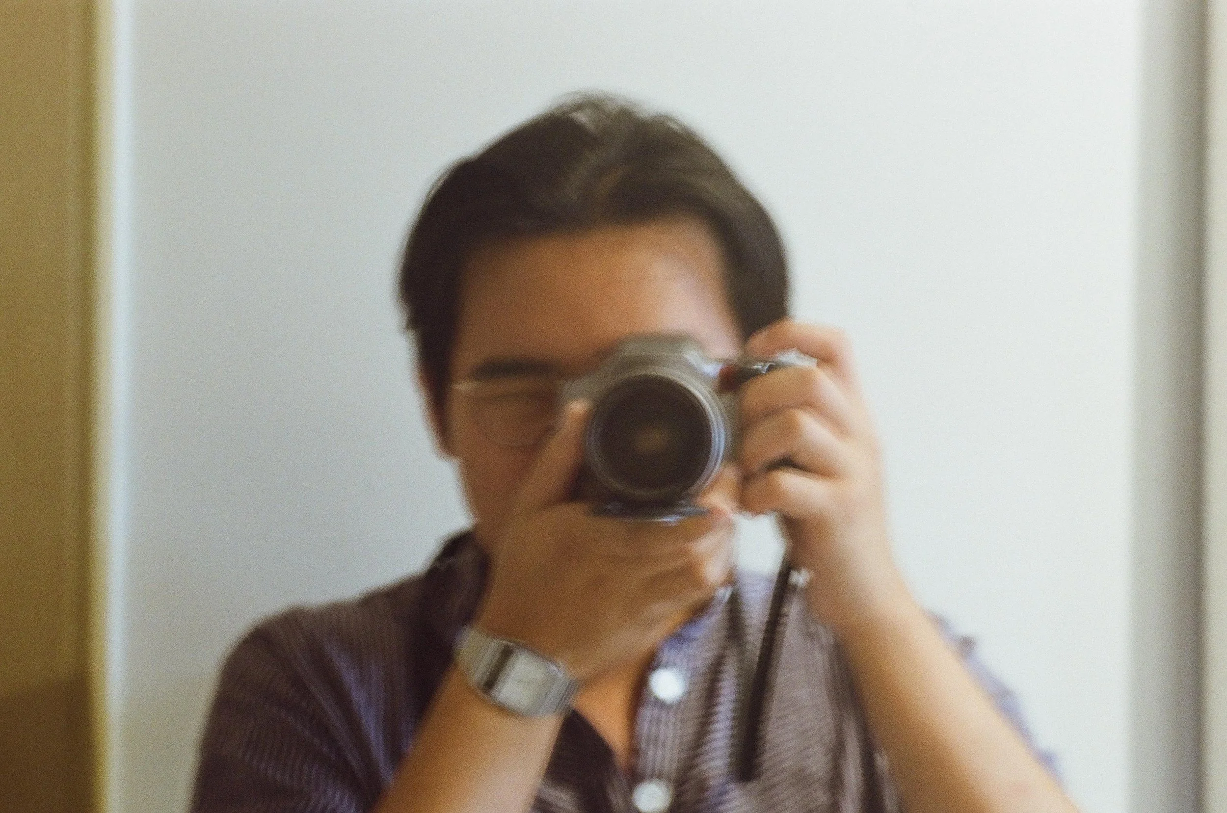 Person taking a photo with a camera in front of a mirror, face partially obscured by the camera.