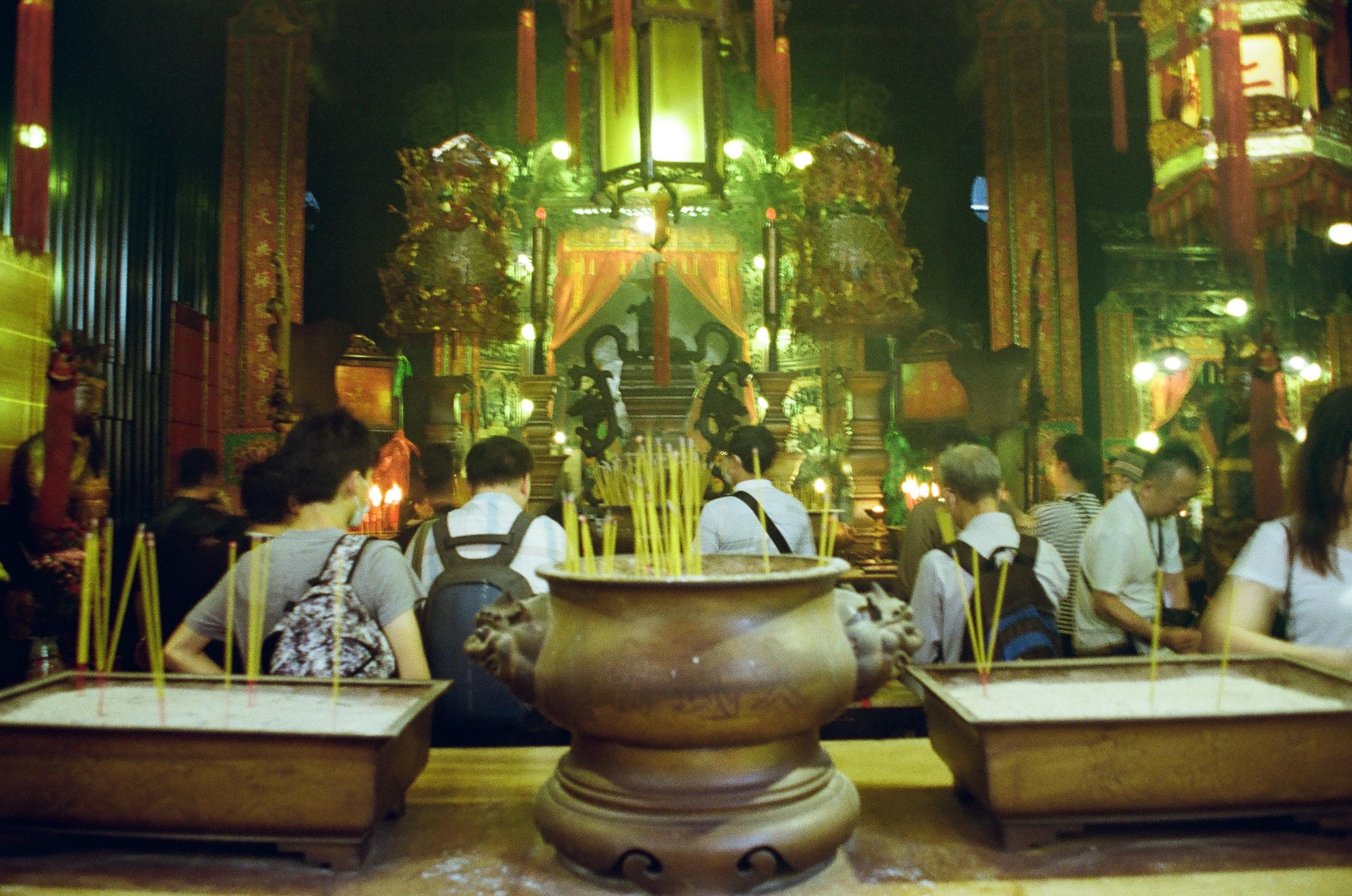 People praying in a temple with incense burners and a richly decorated altar in the background.