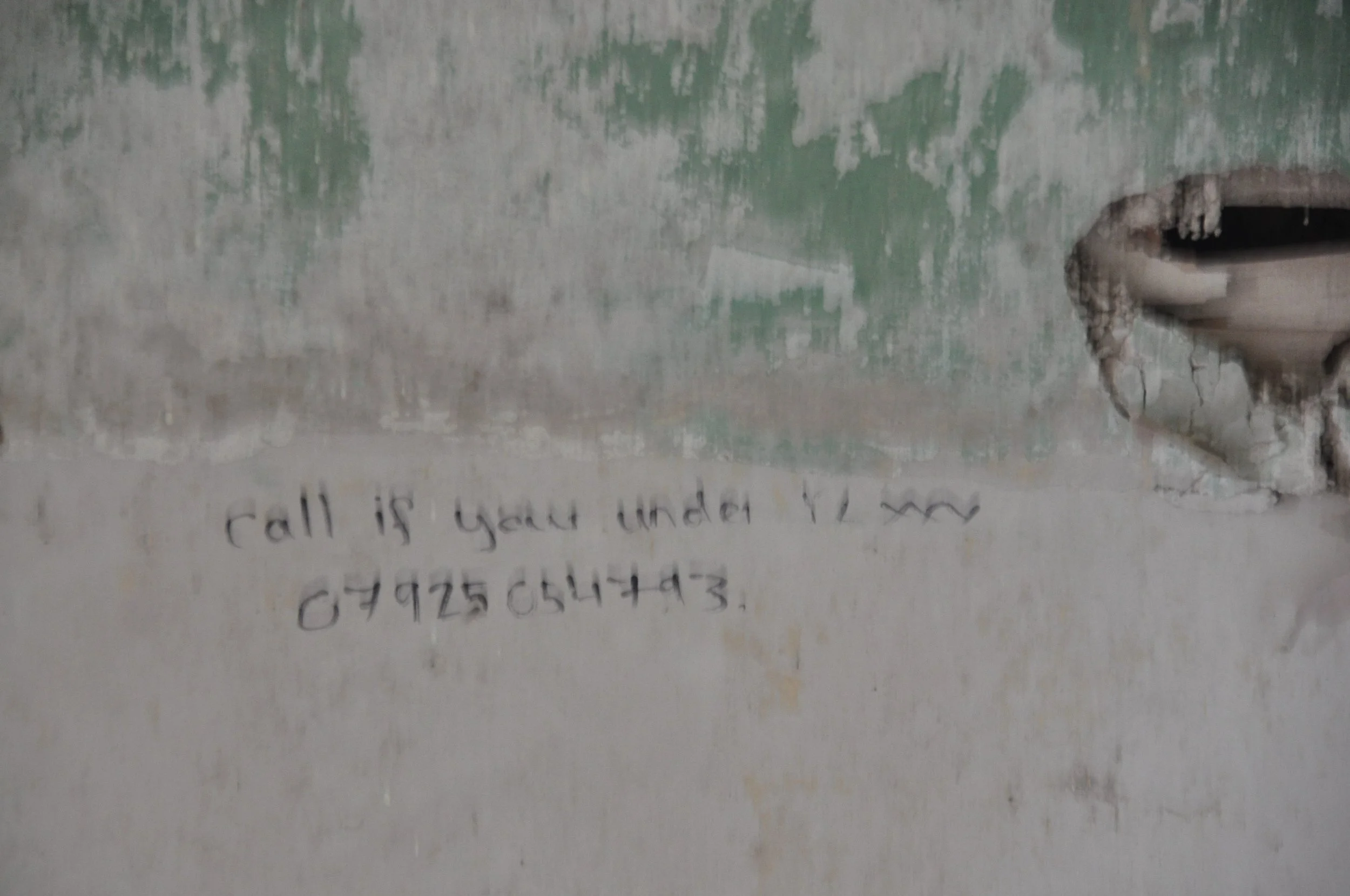 A wall with peeled paint and a hole, with handwritten text that reads, 'call if you are under V2  07925 654443'.
