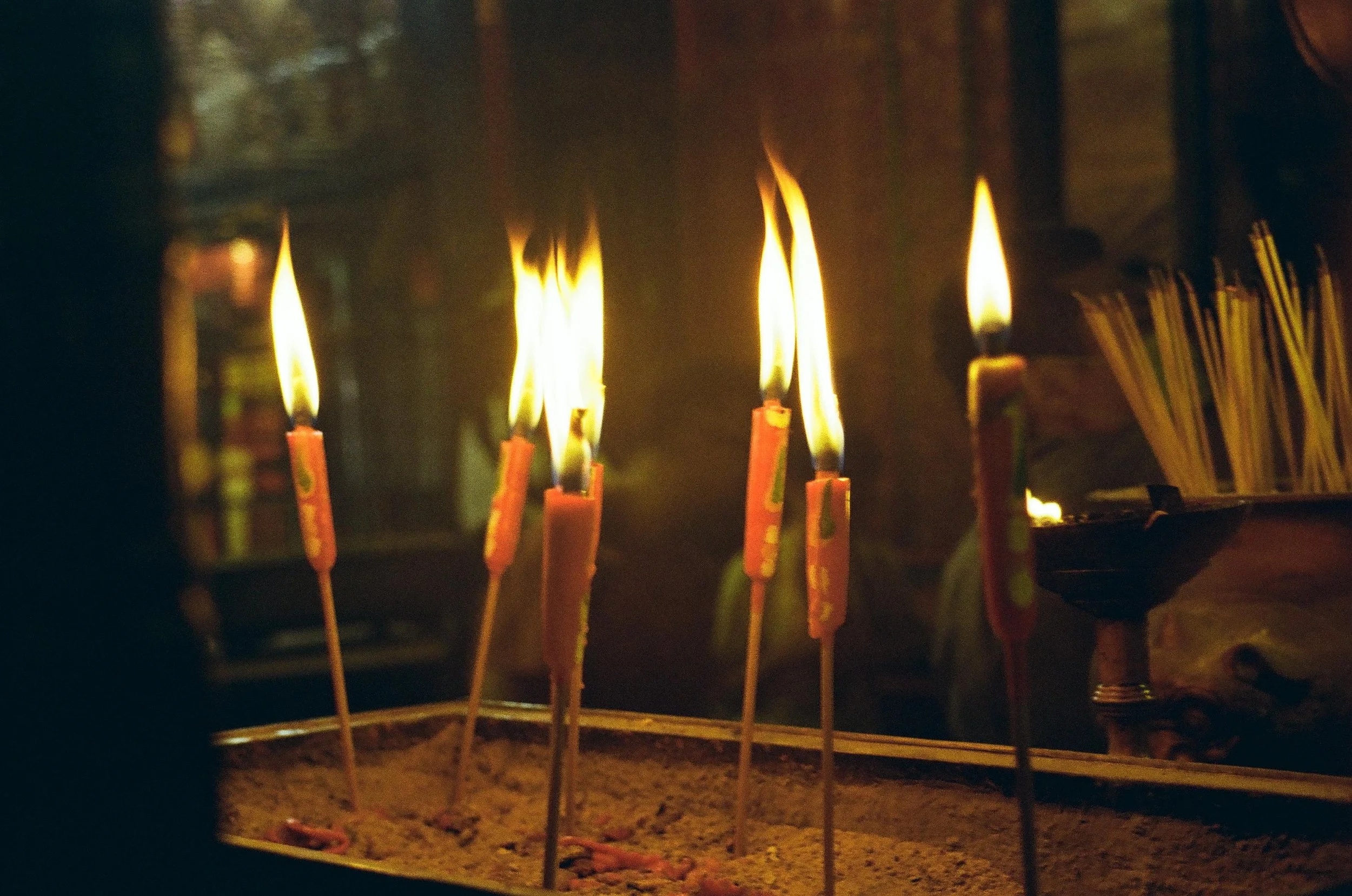 Candles with flames burning in a container filled with sand.