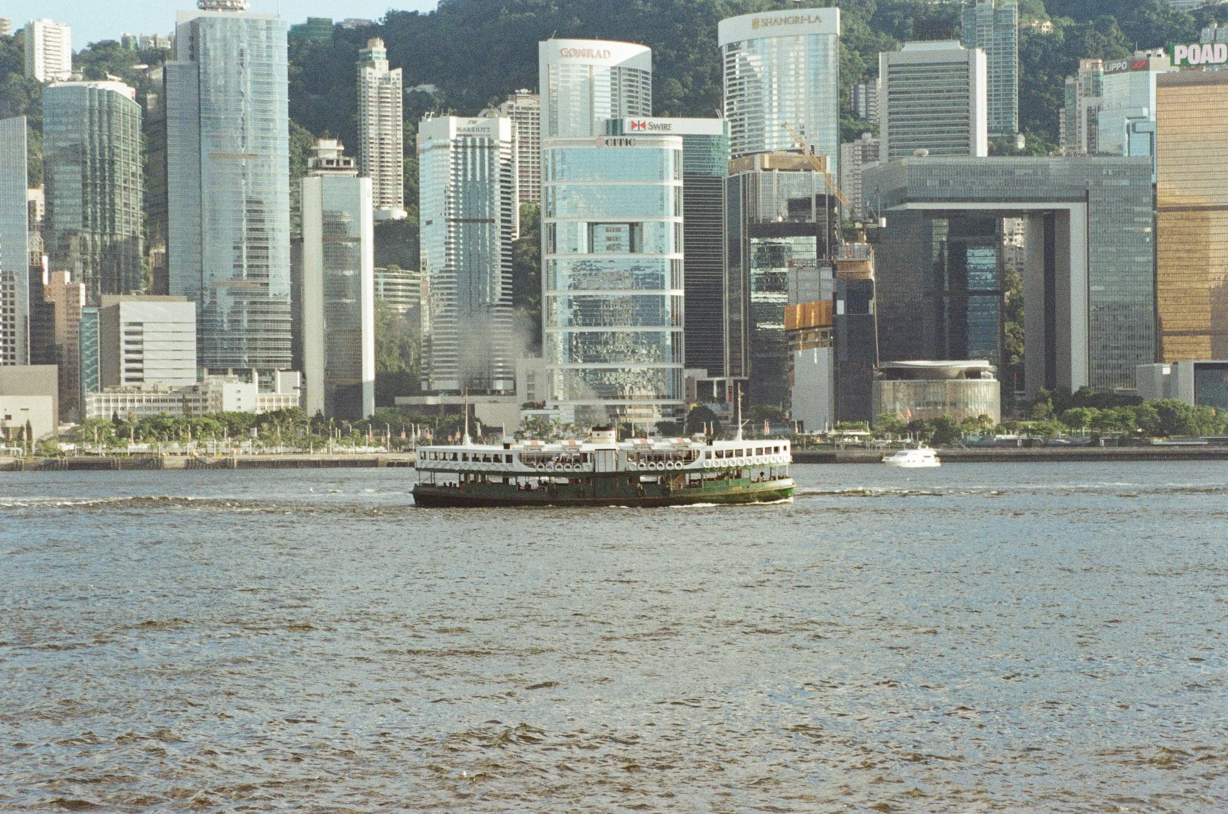 A ferry boat sailing on river with a city skyline in the background, featuring high-rise buildings and skyscrapers.