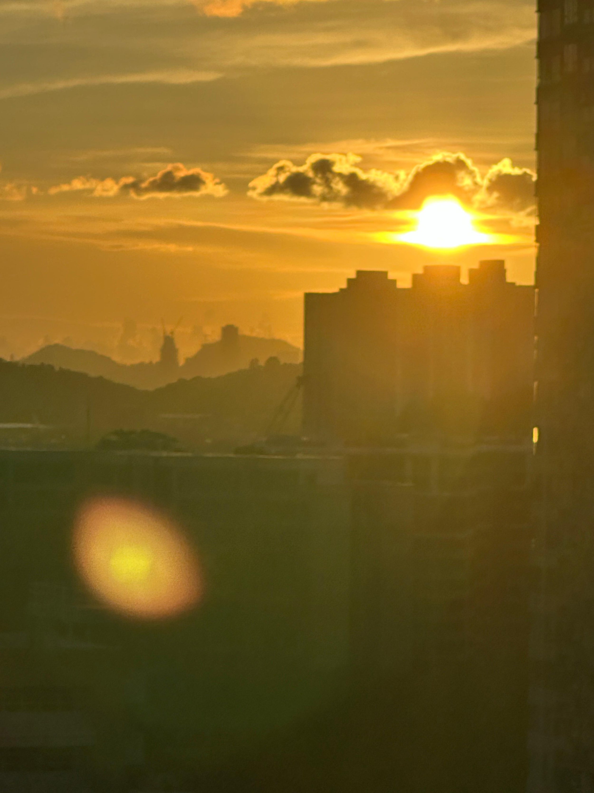 Sunset over city buildings with mountains in the background and clouds in the sky.