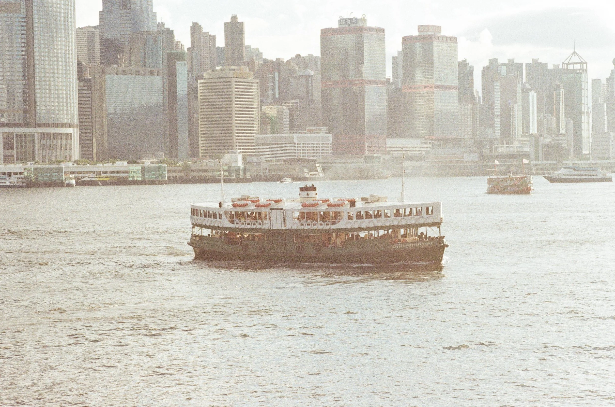 A ferry boat crossing a river with a city skyline in the background.