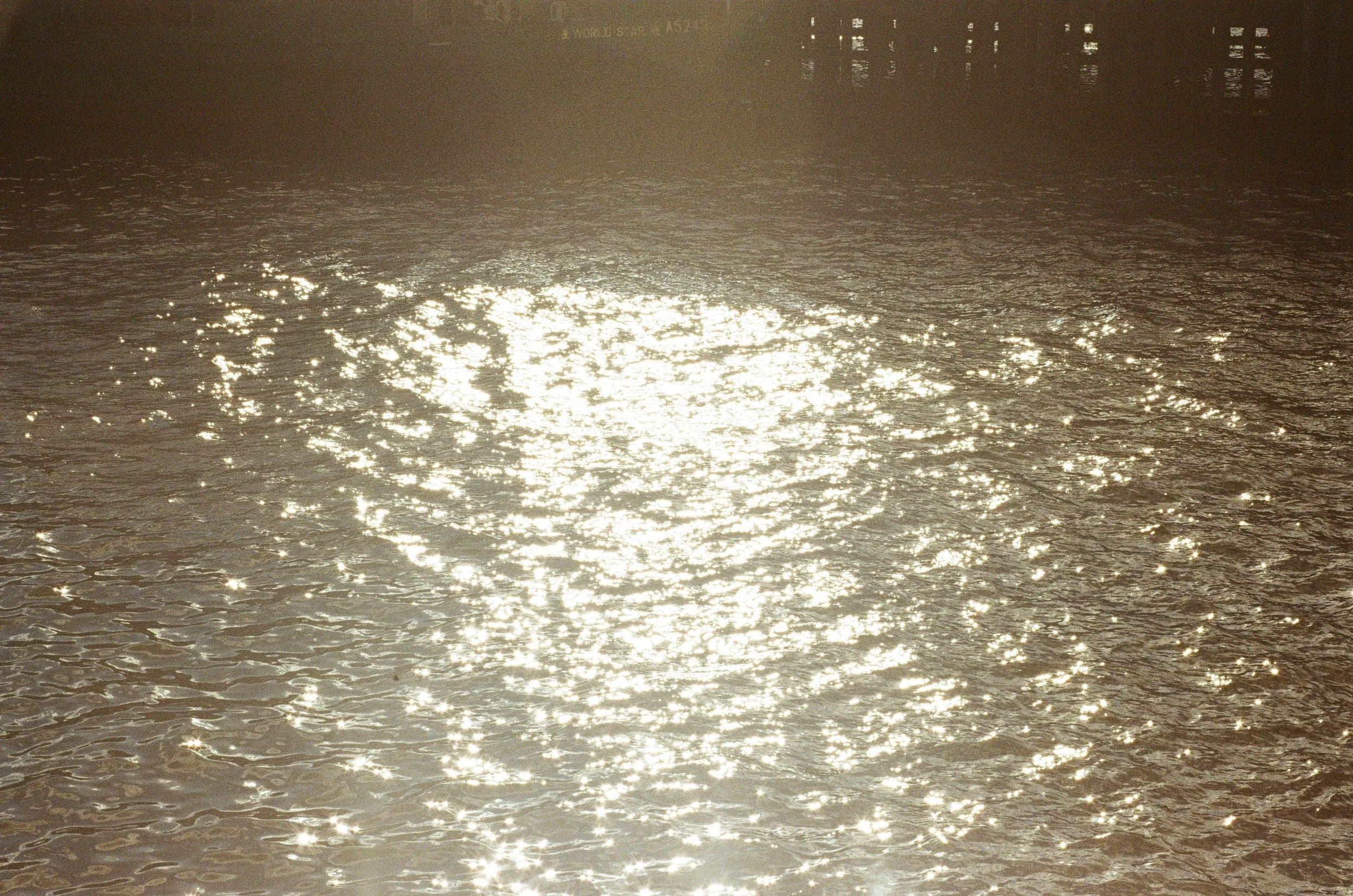 Sunlight reflecting off a body of water with city buildings in the background.
