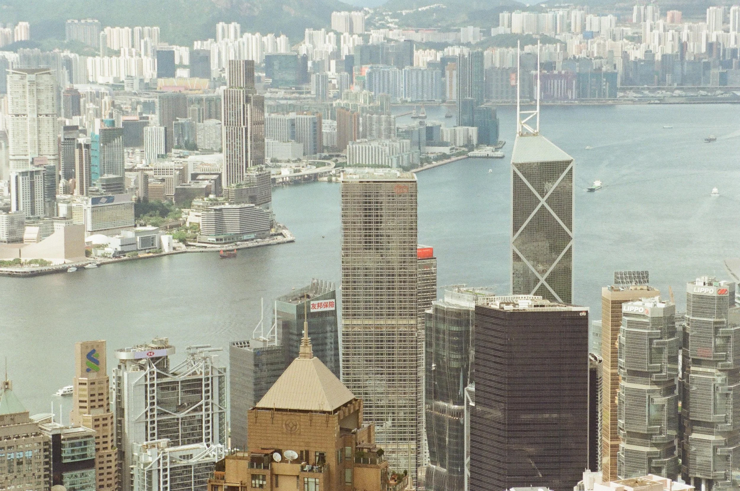 Aerial view of a city skyline featuring tall skyscrapers, a river, and a variety of buildings, with boats on the water and urban landscape in the background.