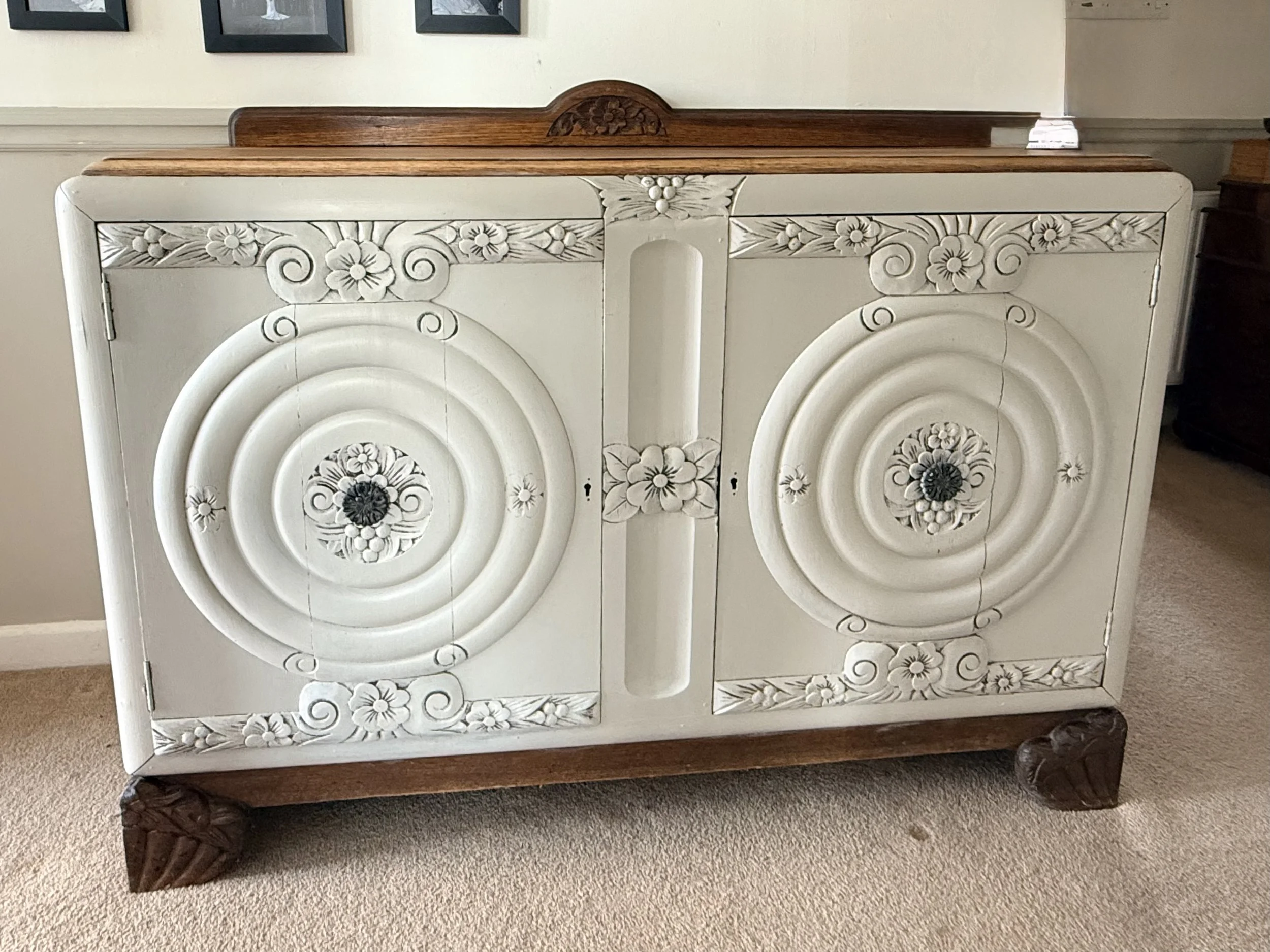 A vintage wooden cabinet with white carved floral designs on the doors and a dark wood top and legs.