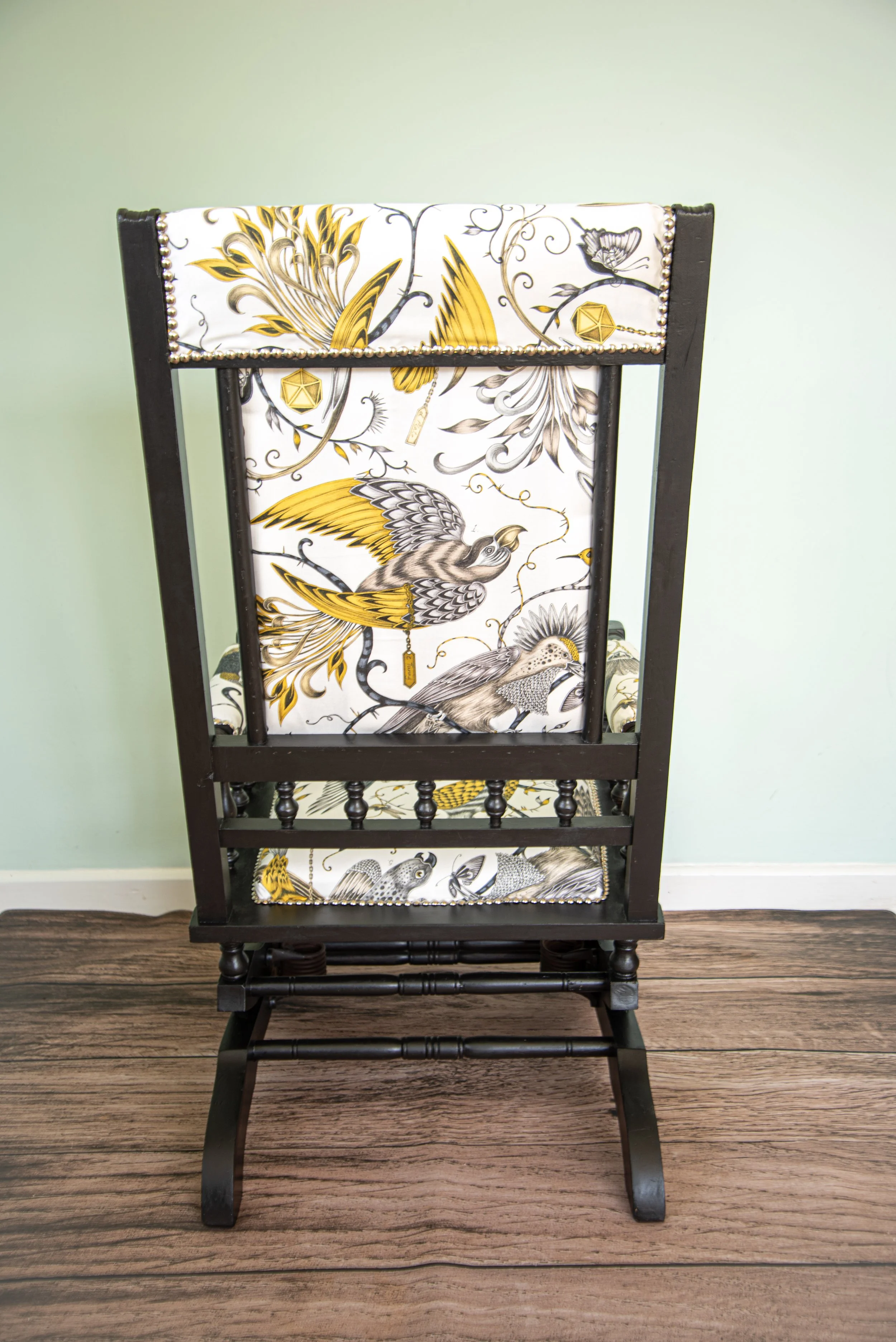 A black wooden rocking chair with a white cushion featuring a bird and floral design in yellow, black, and gray.